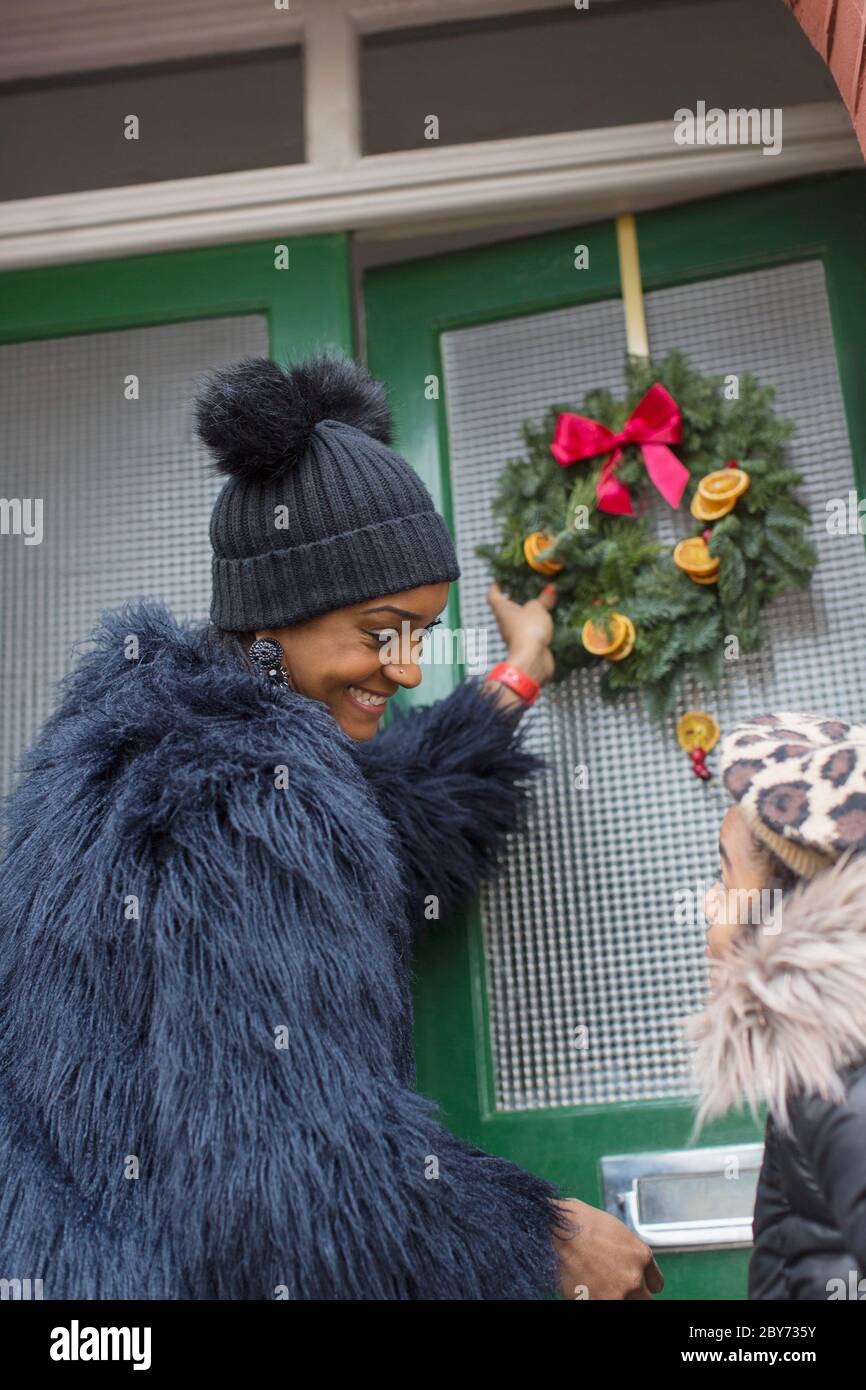 Glückliche Mutter und Tochter hängen Weihnachtskranz an der Haustür Stockfoto