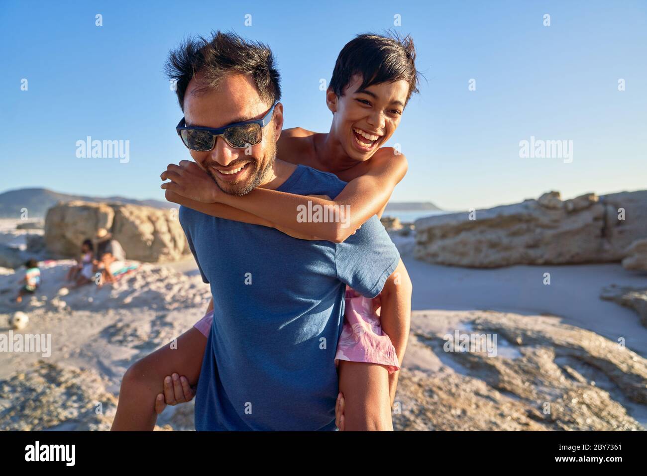 Glücklicher Vater Huckepack Sohn am sonnigen Strand Stockfoto