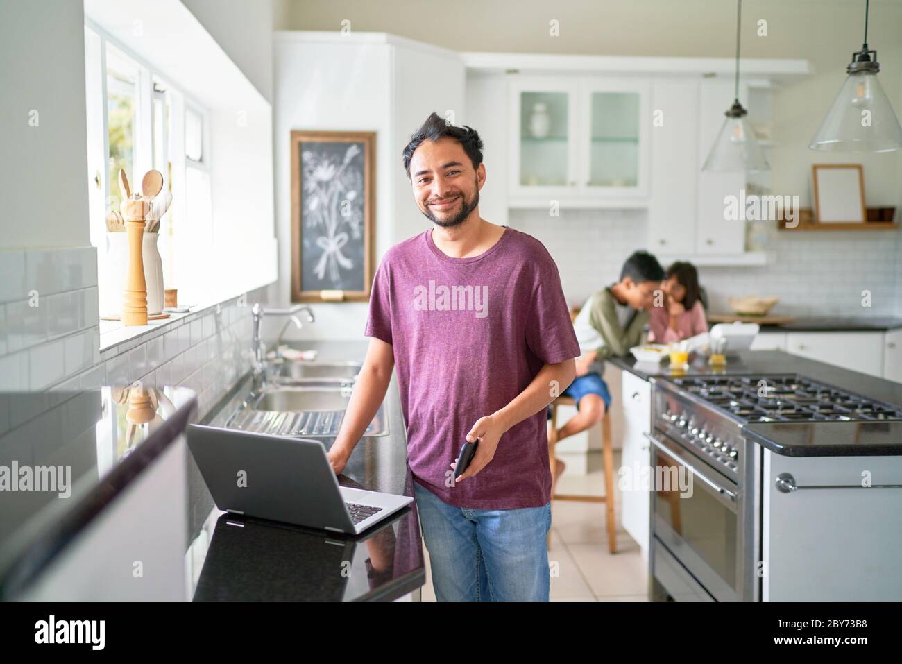 Portrait glücklicher Vater arbeitet am Laptop in der Küche mit Kindern essen Stockfoto