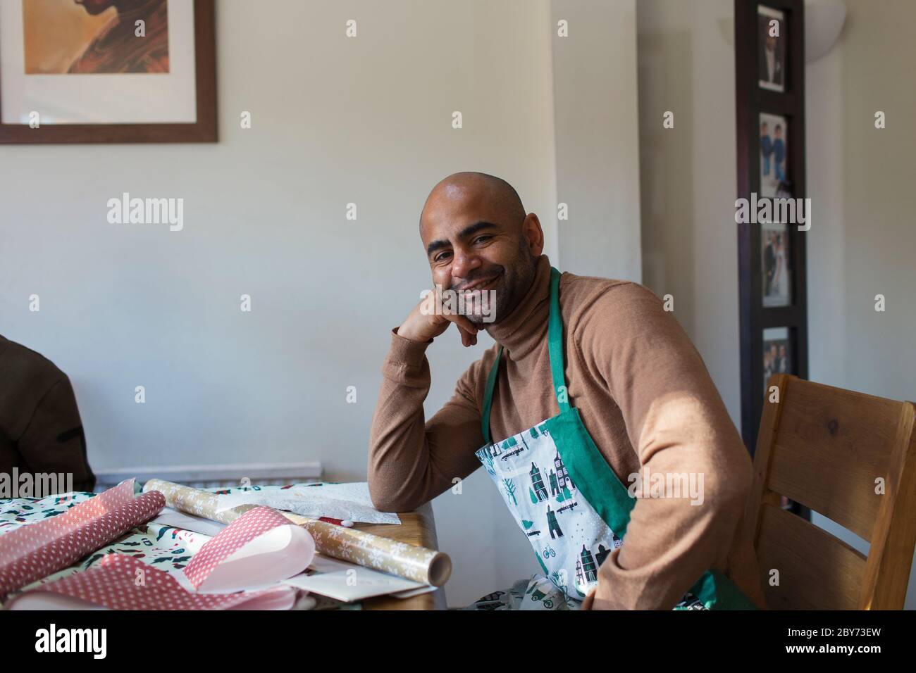 Portrait glücklicher Mann in Weihnachten Schürze Geschenkverpackung am Tisch Stockfoto
