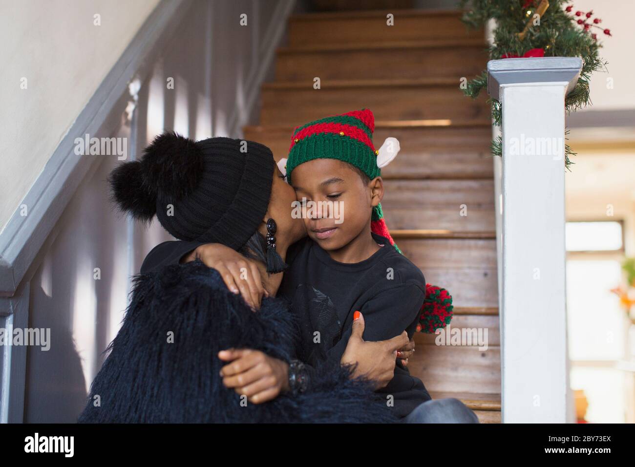 Liebevolle Mutter küsst Sohn in Weihnachtshut auf Treppen Stockfoto