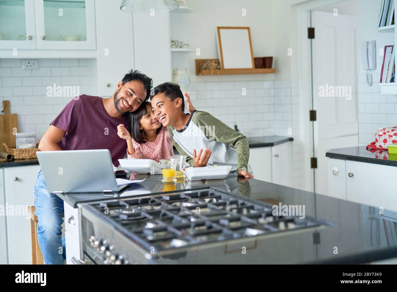 Verspielte Vater und Kinder essen und mit Laptop in der Küche Stockfoto