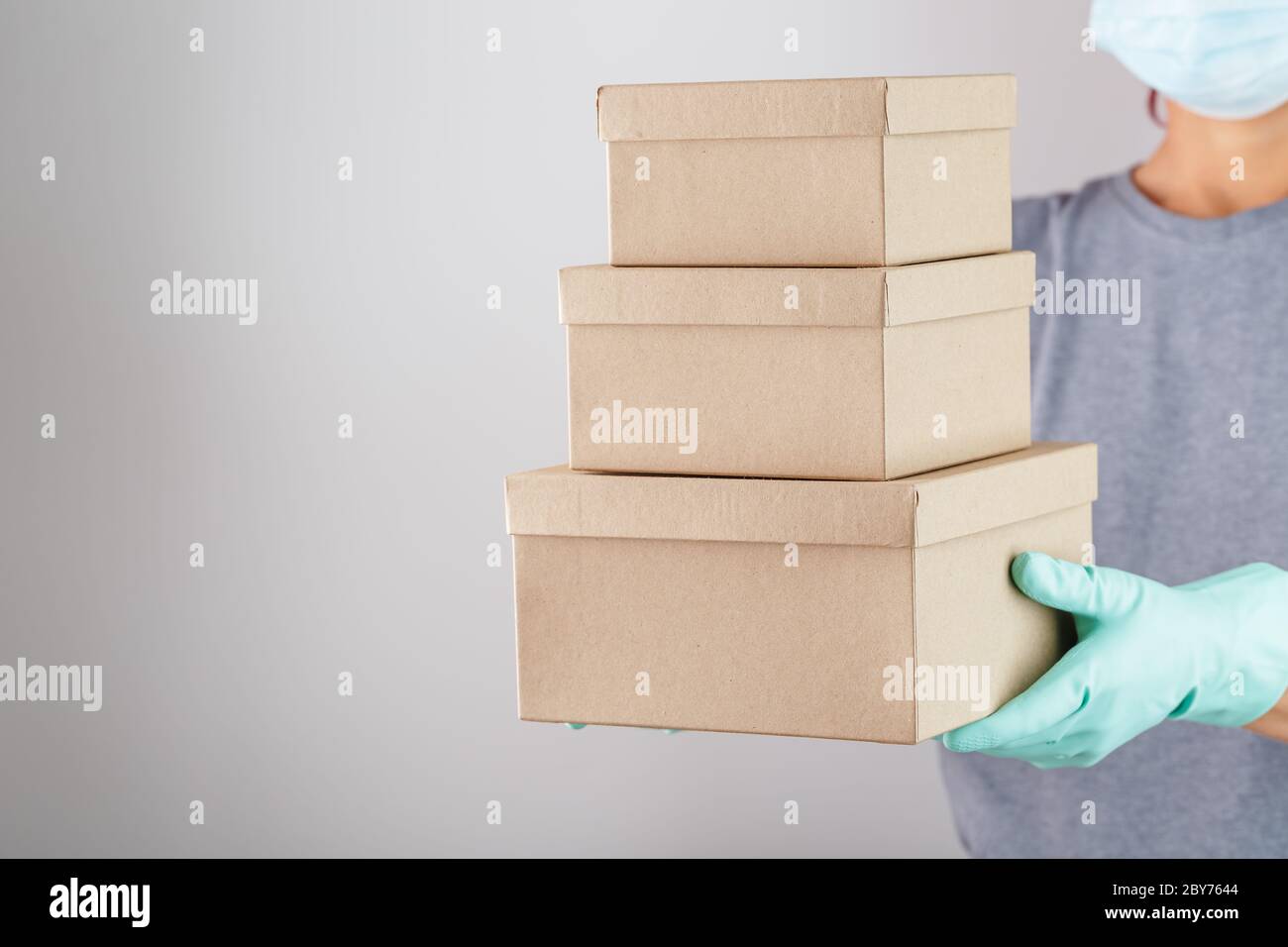 Der Kurier hält ein Paket von Kartons mit blauen Gummihandschuhen in der Hand. Stockfoto