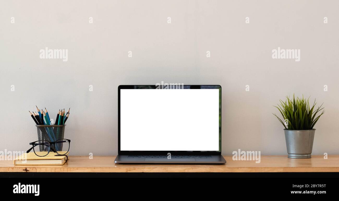 Kurzer Schnitt des einfachen Arbeitsbereichs mit leerem Bildschirm, Laptop, Tasse, Schreibwaren und Kopierfläche Stockfoto