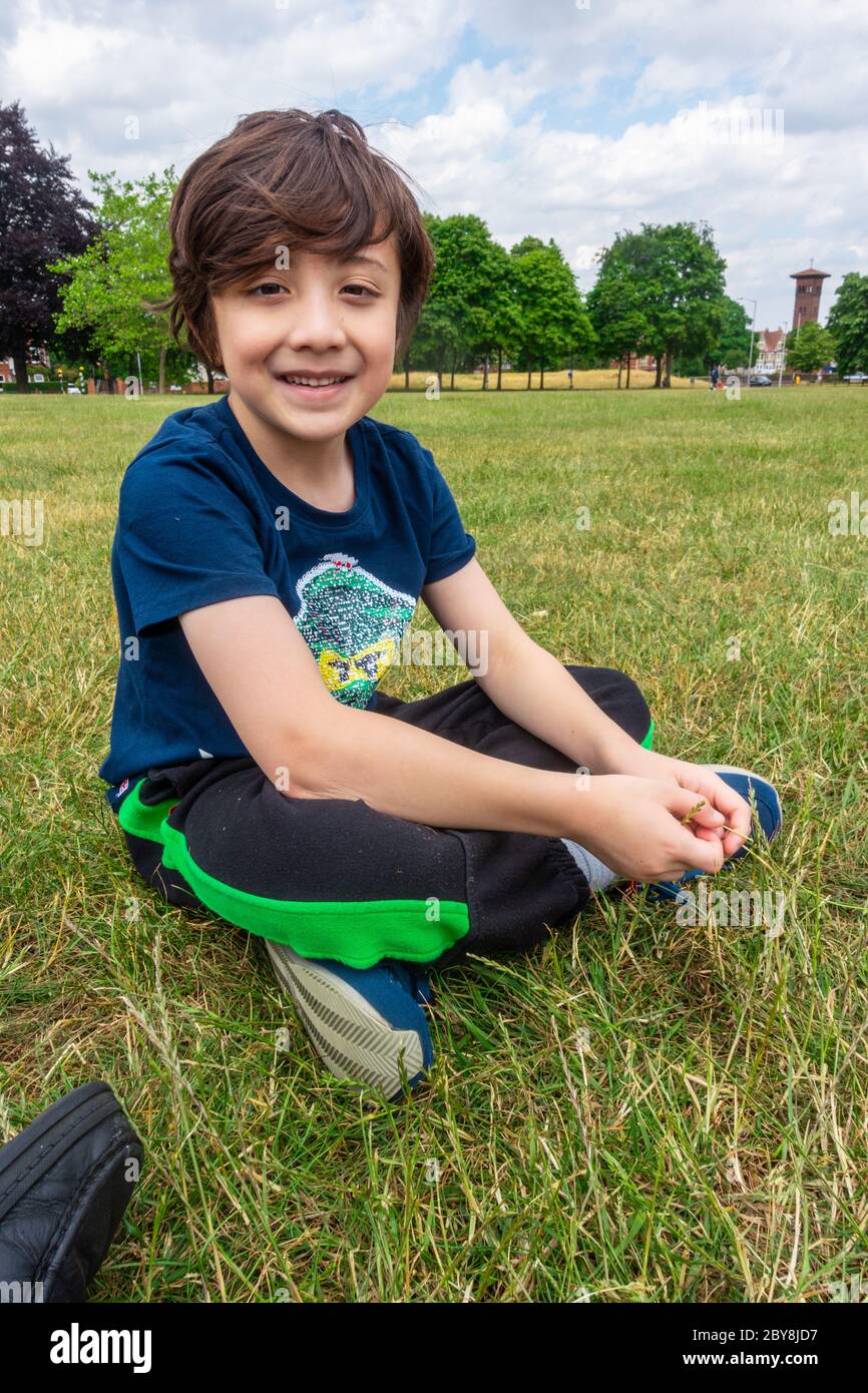 Ein kleiner Junge sitzt auf dem Boden im Park, lächelt und posiert für ein Porträt. Stockfoto
