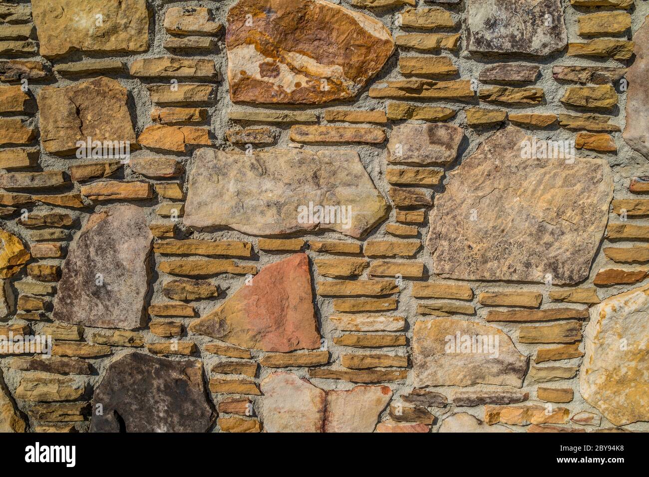 Vielfalt von Felsen in einem gestapelten Muster mit verschiedenen Formen und Größen mit Mörtel dazwischen für eine Wand eines Gebäudes im Freien an einem hellen sonnigen Tag Stockfoto