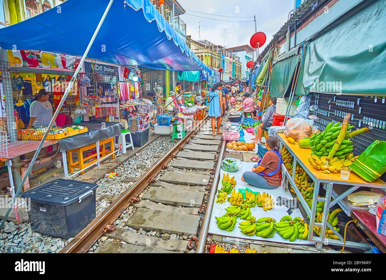 MAEKLONG, THAILAND - 13. MAI 2019: Die Straßenhändler sitzen auf dem Boden an der Eisenbahn des Maeklong Railway Market und bieten frisches Obst und Gemüse an Stockfoto