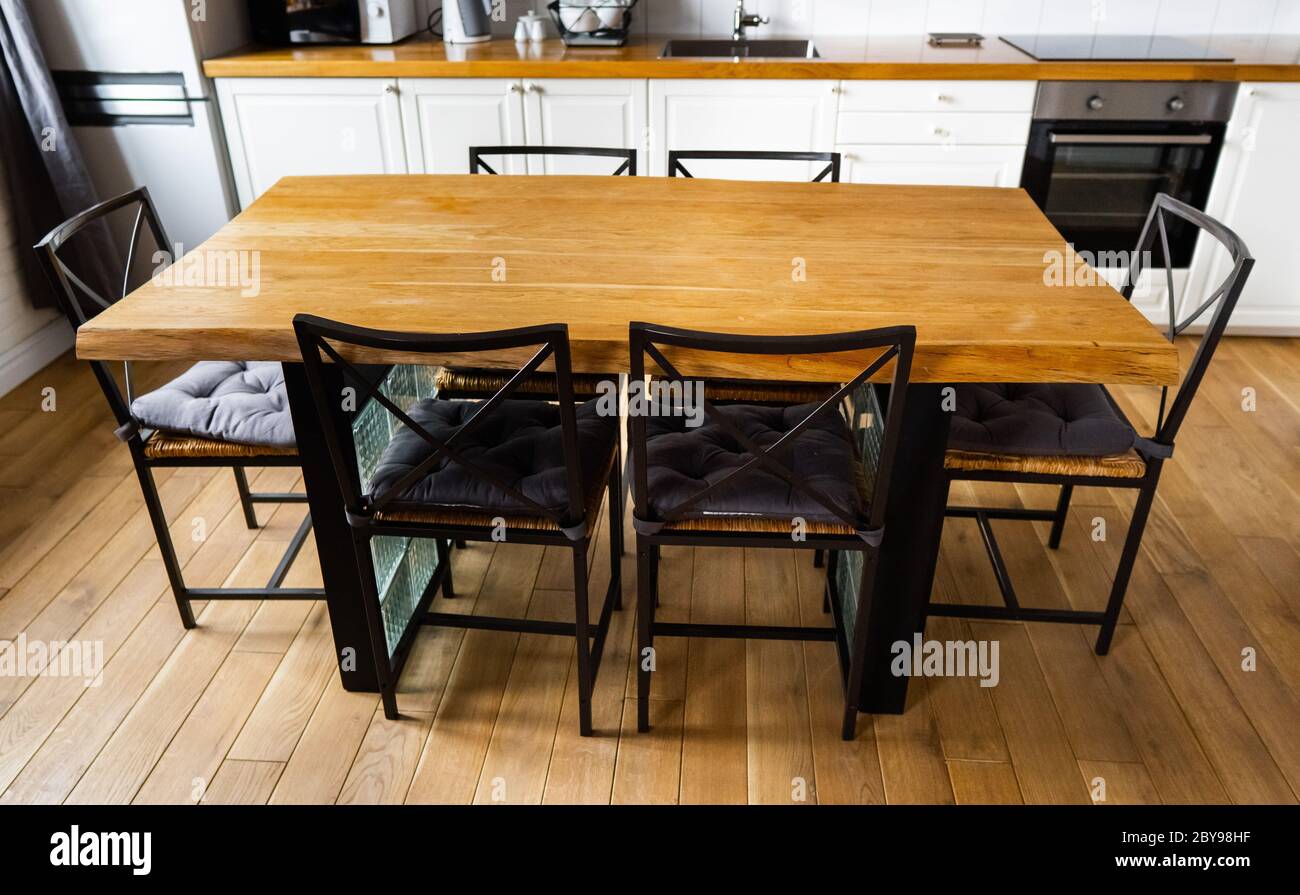 Ein großer Esstisch aus Holz mit Glasblöcken und Rattanstühlen aus Metall und Kissen in moderner skandinavischer und Wohnküche, gegen helles Weiß Stockfoto