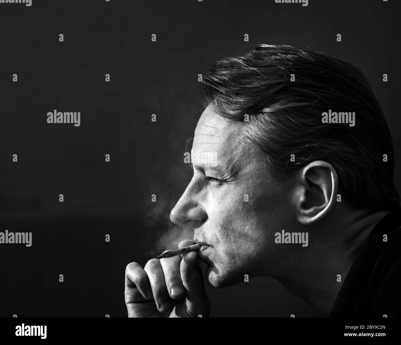 Ein Mann mit einer Zigarette. Harter Kontrast des Sonnenlichts. Rauchen und Gesundheit. Schwarz und Weiß. Stockfoto