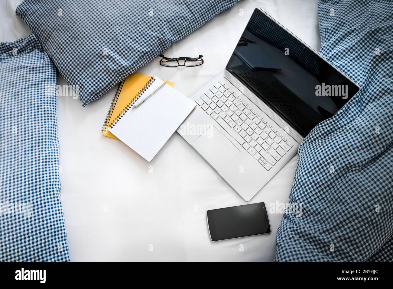 WFH - Arbeit von zu Hause Laptop, Notizblock und Handy auf Bett 1 Stockfoto