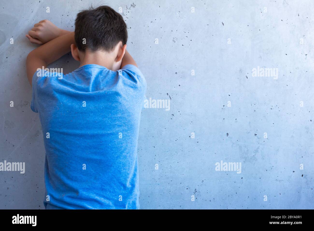 Verärgert trauriger Junge stehen allein zurück und lehnen sich an die Wand. Lernschwierigkeiten, familiäre Probleme, Mobbing, Depression, Stress oder Frustration Konzept Stockfoto