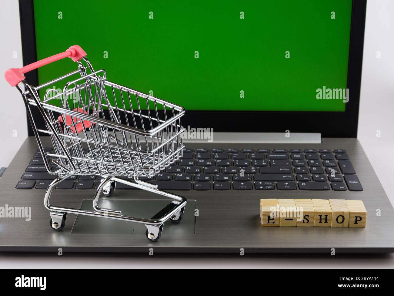 E - Shop gefaltet mit Würfeln mit Buchstaben auf dem Hintergrund eines Laptops und Trolley 3 Stockfoto