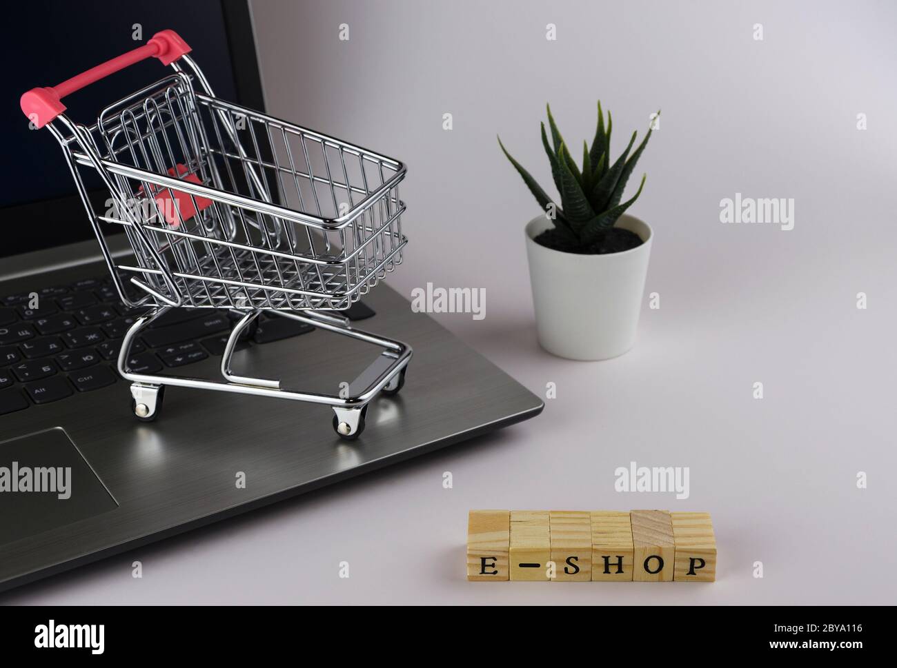 E - Shop gefaltet mit Würfeln mit Buchstaben auf dem Hintergrund eines Laptops und Trolley 4 Stockfoto
