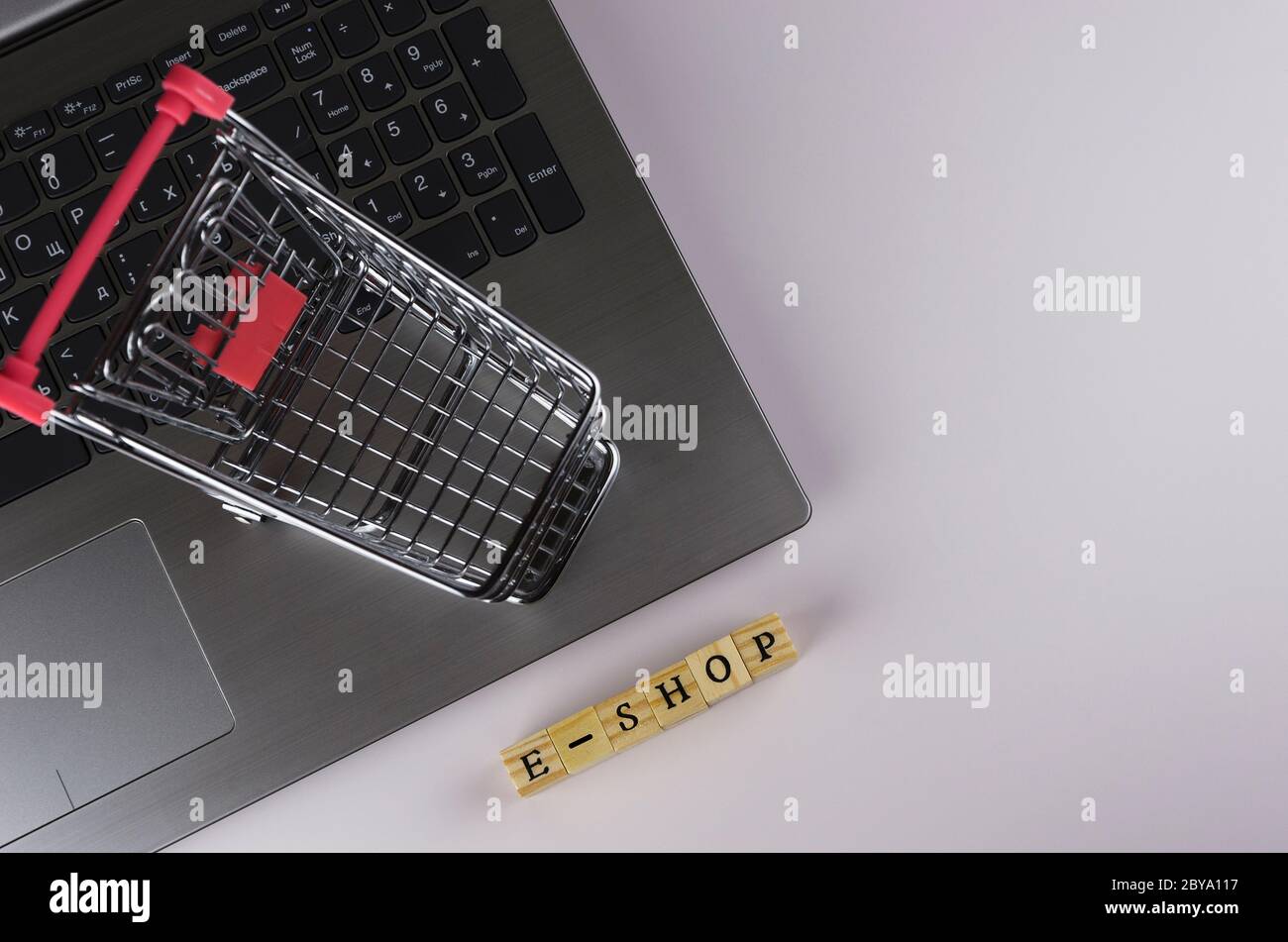 E - Shop gefaltet mit Würfeln mit Buchstaben auf dem Hintergrund eines Laptops und Trolley Stockfoto
