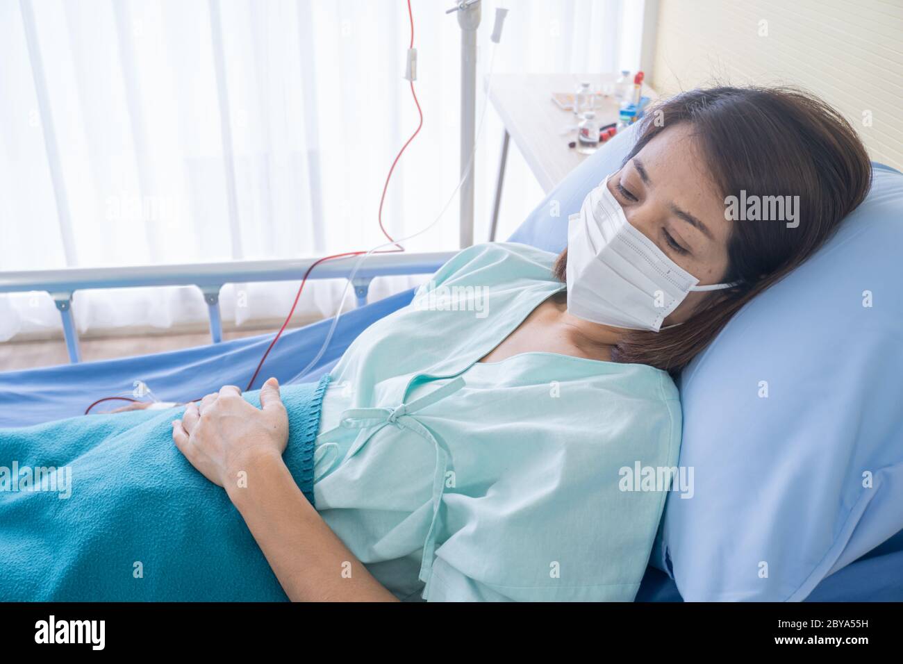 Asiatische Frau ist krank hat hohes Fieber, Niesen, erholt sich im Kleid  des Patienten auf dem Patientenbett im Krankenhaus mit Gesichtsmasken zu  schützen lag Stockfotografie - Alamy