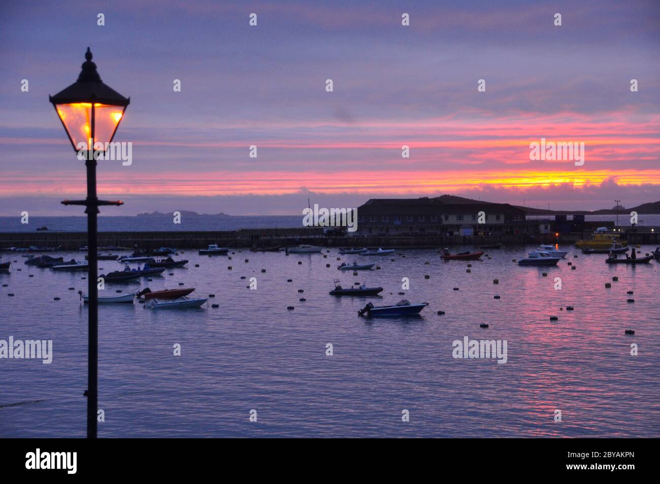 Sonnenuntergang über St Marys Hafen auf die Scilly-inseln, Lamp Post spiegelt die untergehende Sonne. Cornwall GROSSBRITANNIEN Stockfoto