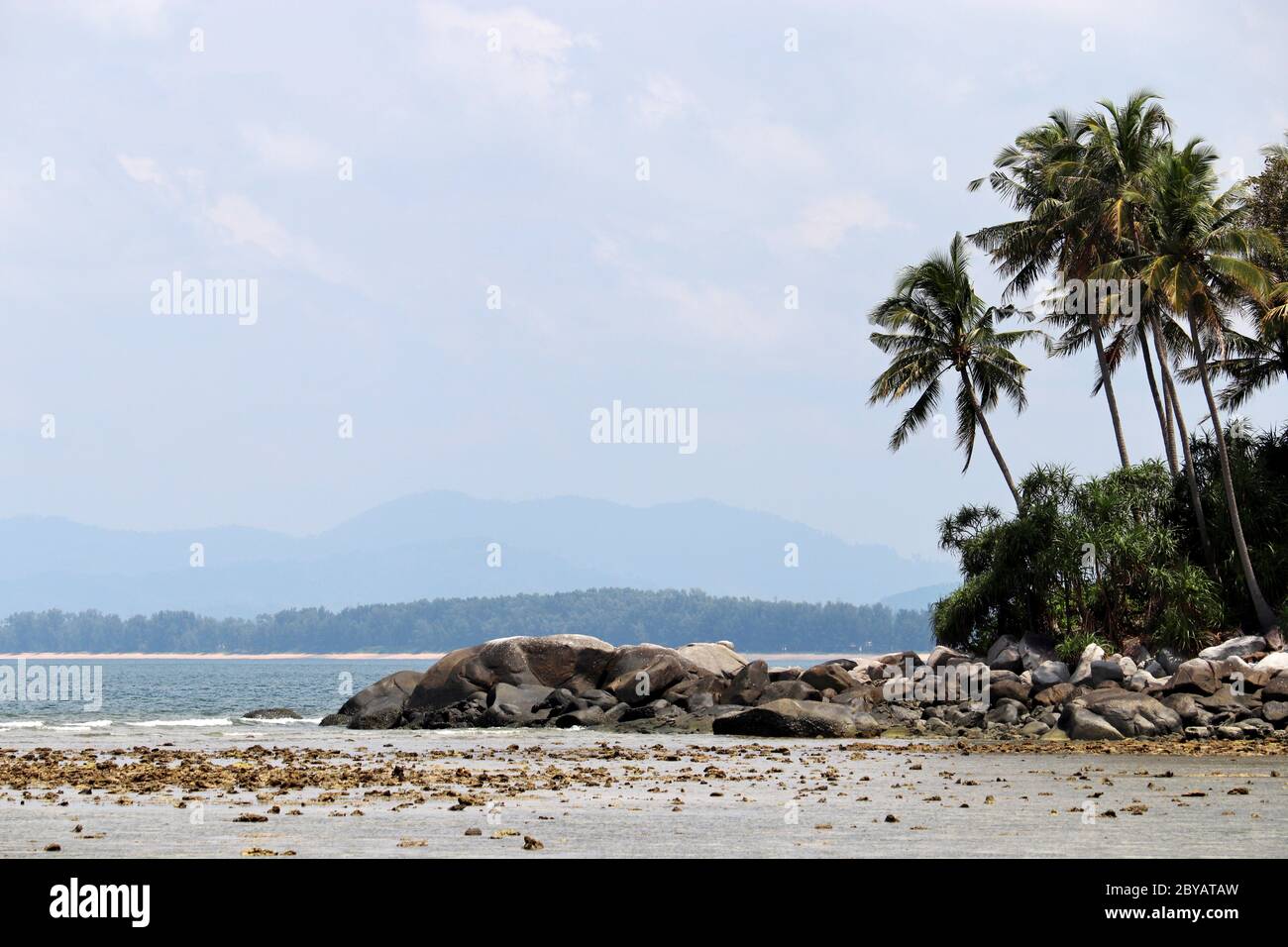 Tropische Insel mit Kokospalmen im Meer, Strand mit Felsen, malerischer Blick auf Berge im Nebel. Konzept des Urlaubs auf paradiesischen Natur Stockfoto