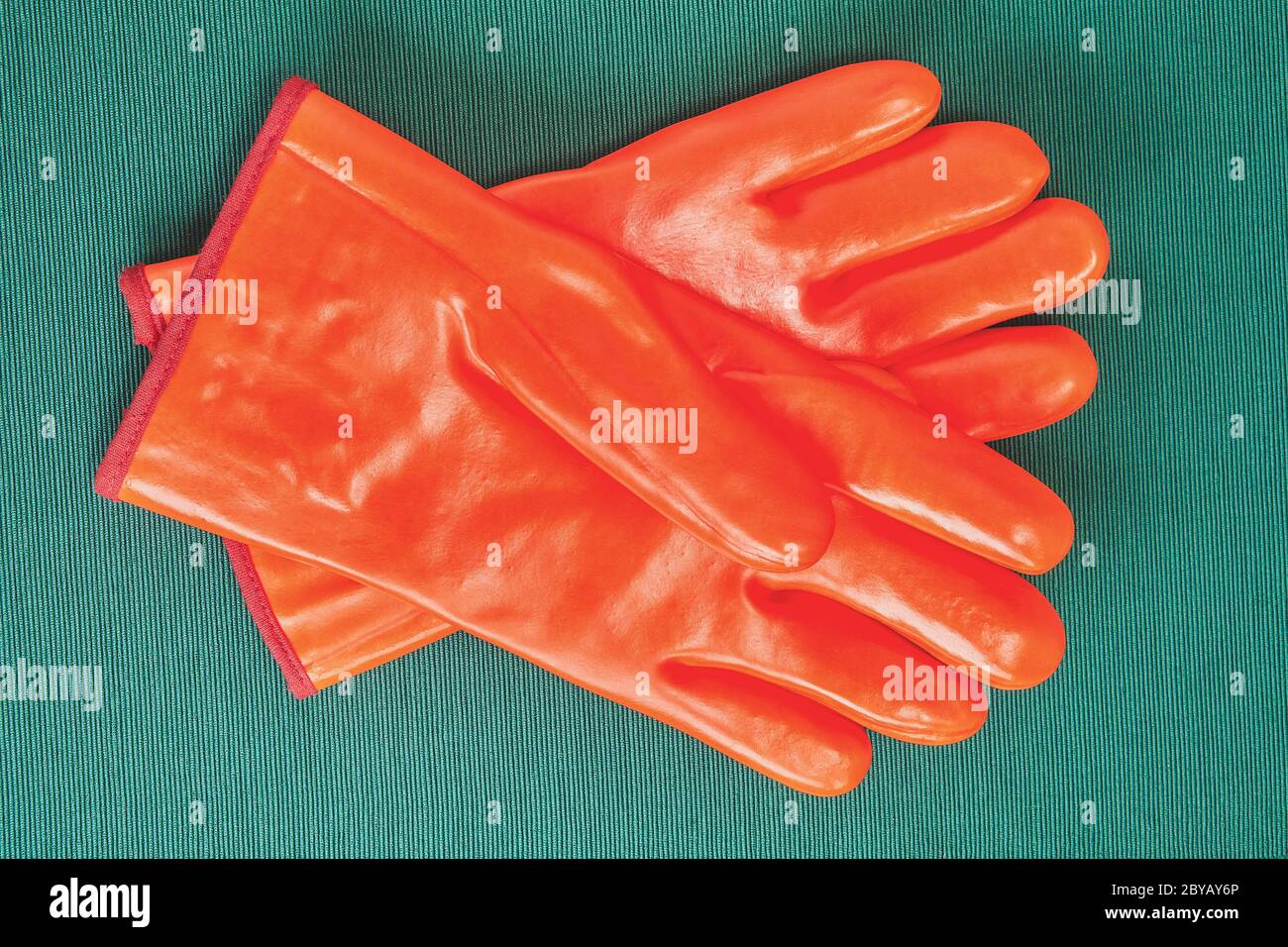 Orangefarbene chemikalienbeständige Handschuhe mit Schutz vor kalter, industrieller Schutzkleidung, auf grünem Hintergrund. Stockfoto