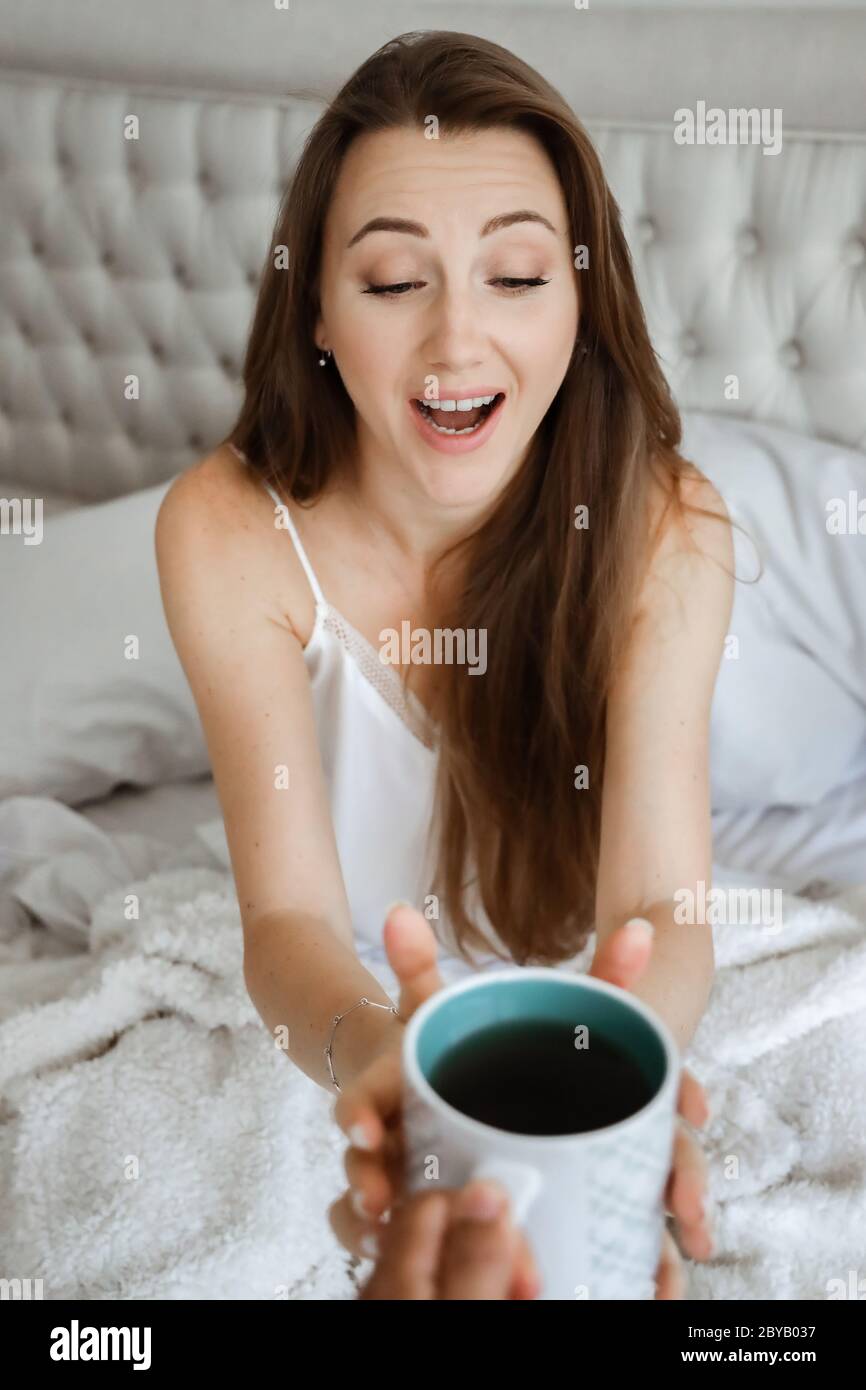 Frau im Bett trinkt Kaffee. Glückliches Mädchen. Morgenkonzept. Frühstück im Bett Stockfoto
