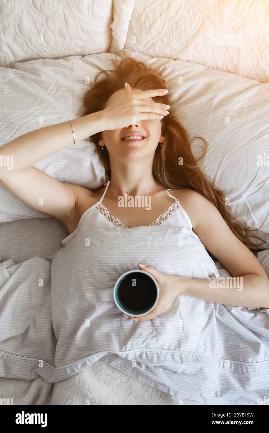 Frau im Bett trinkt Kaffee. Glückliches Mädchen. Morgenkonzept. Frühstück im Bett Stockfoto