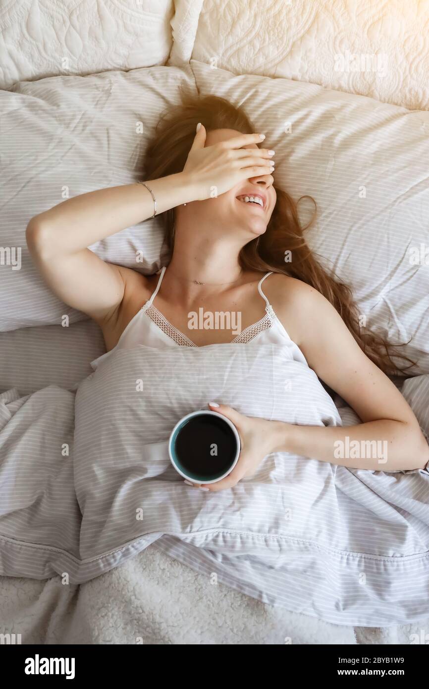 Frau im Bett trinkt Kaffee. Glückliches Mädchen. Morgenkonzept. Frühstück im Bett Stockfoto