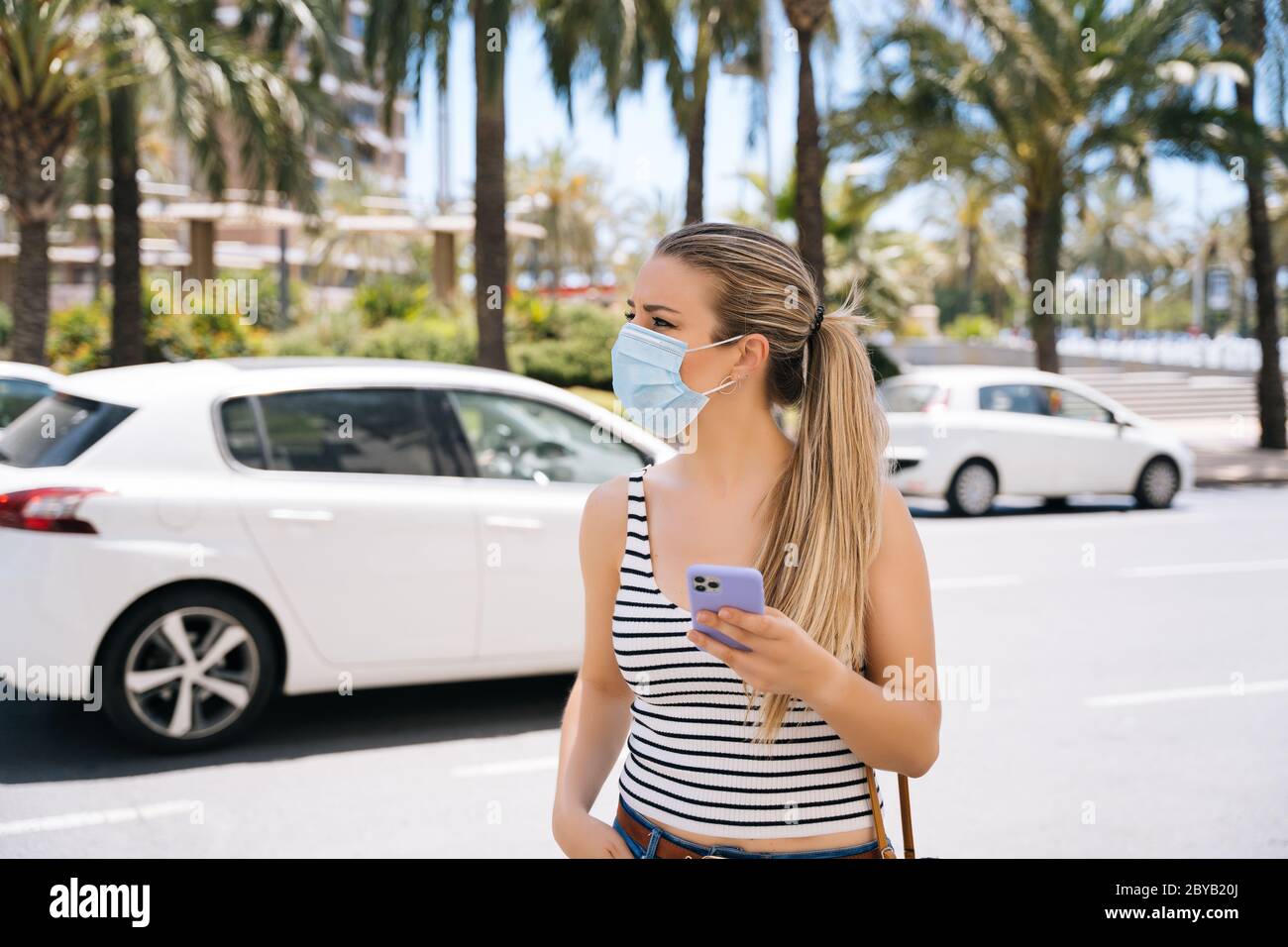 Frau in Maske in der Stadt mit ihrem Handy während der Coronavirus-Pandemie Stockfoto