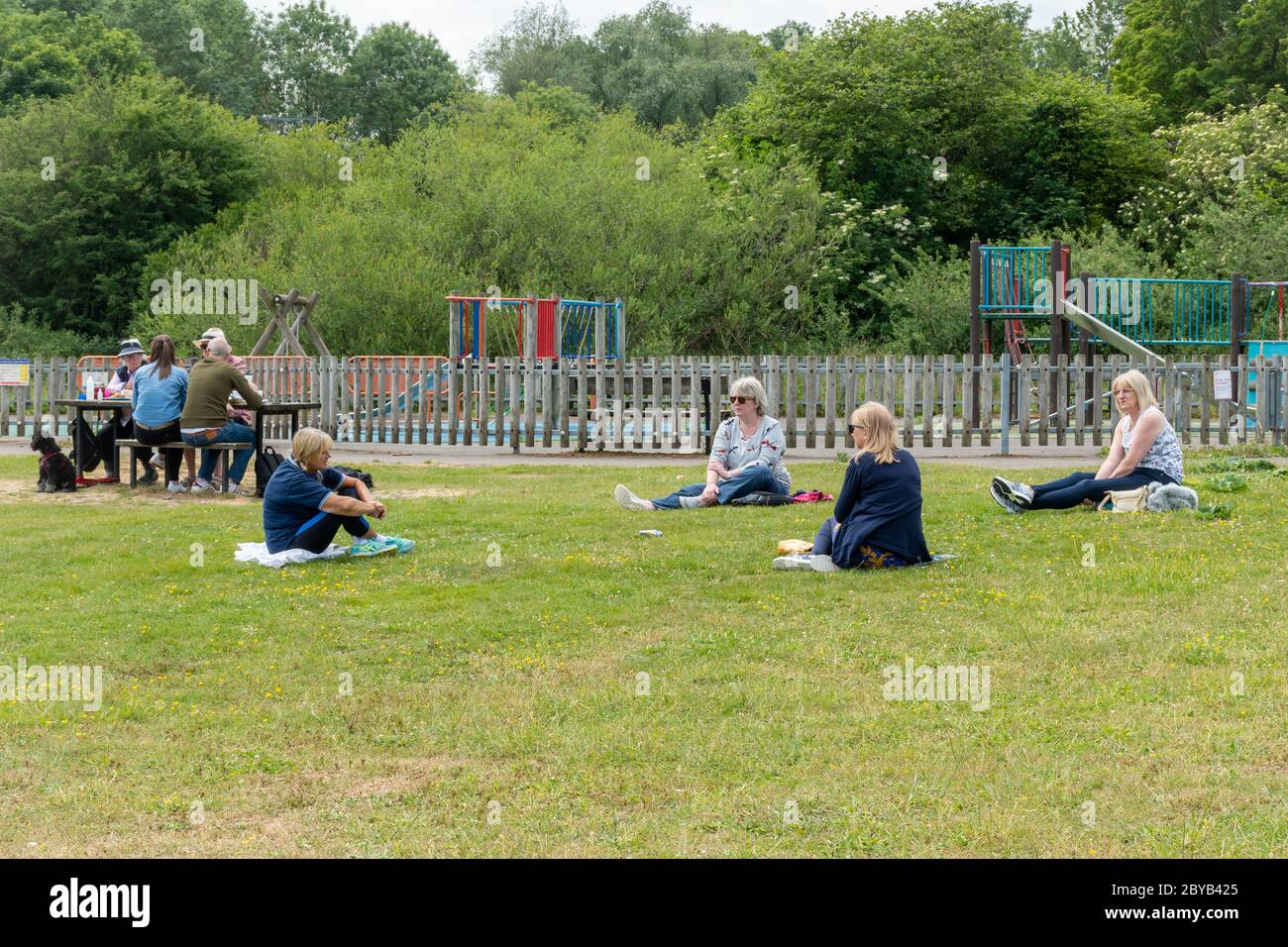 Eine Gruppe von vier Frauen, die in einem Park mit sozialer Distanz sitzen, 2 Meter voneinander entfernt, nachdem die Sperrung des Coronavirus Covid-19 erleichtert wurde, Großbritannien, Juni 2020 Stockfoto