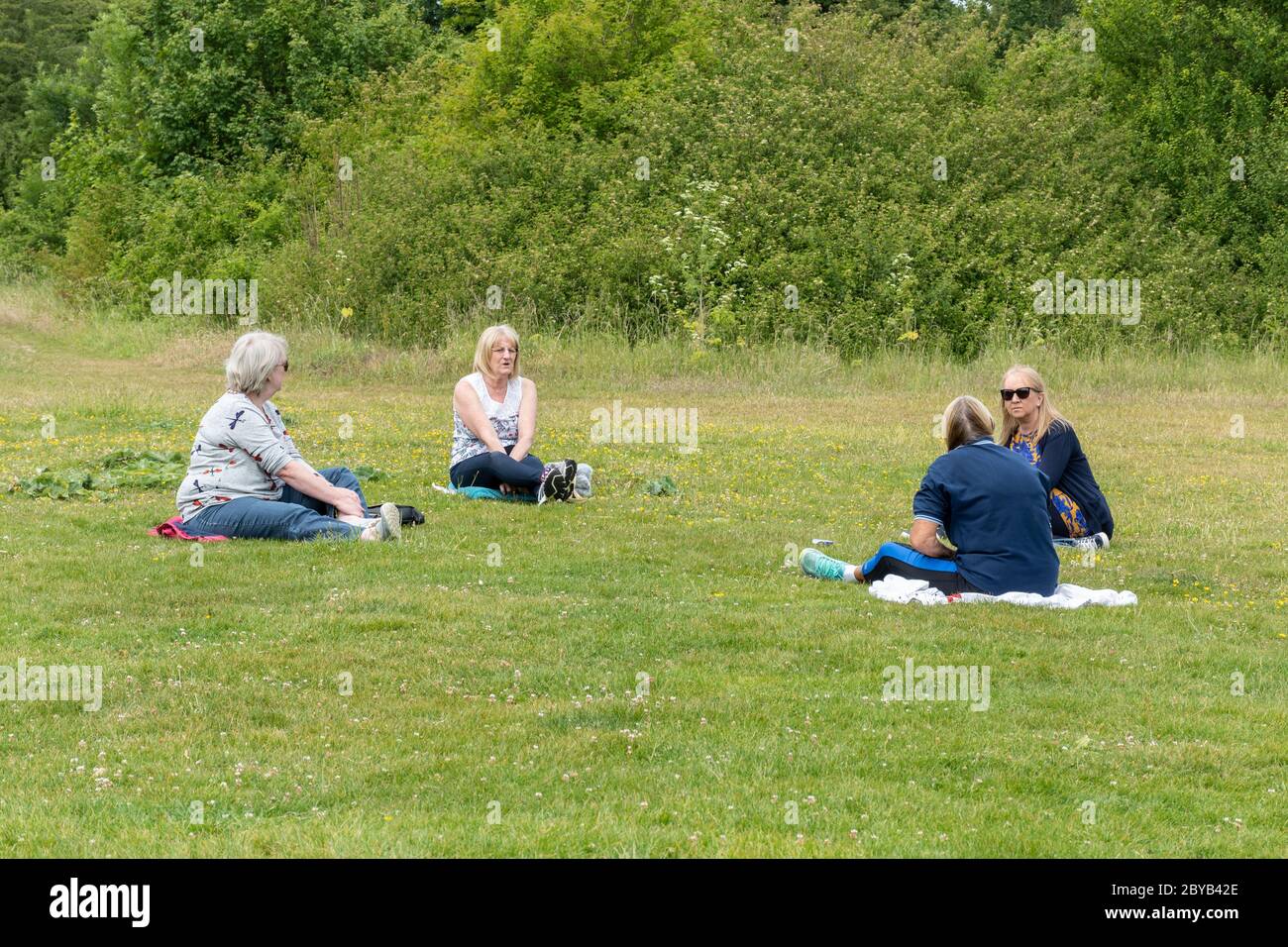 Eine Gruppe von vier Frauen, die in einem Park mit sozialer Distanz sitzen, 2 Meter voneinander entfernt, nachdem die Sperrung des Coronavirus Covid-19 erleichtert wurde, Großbritannien, Juni 2020 Stockfoto