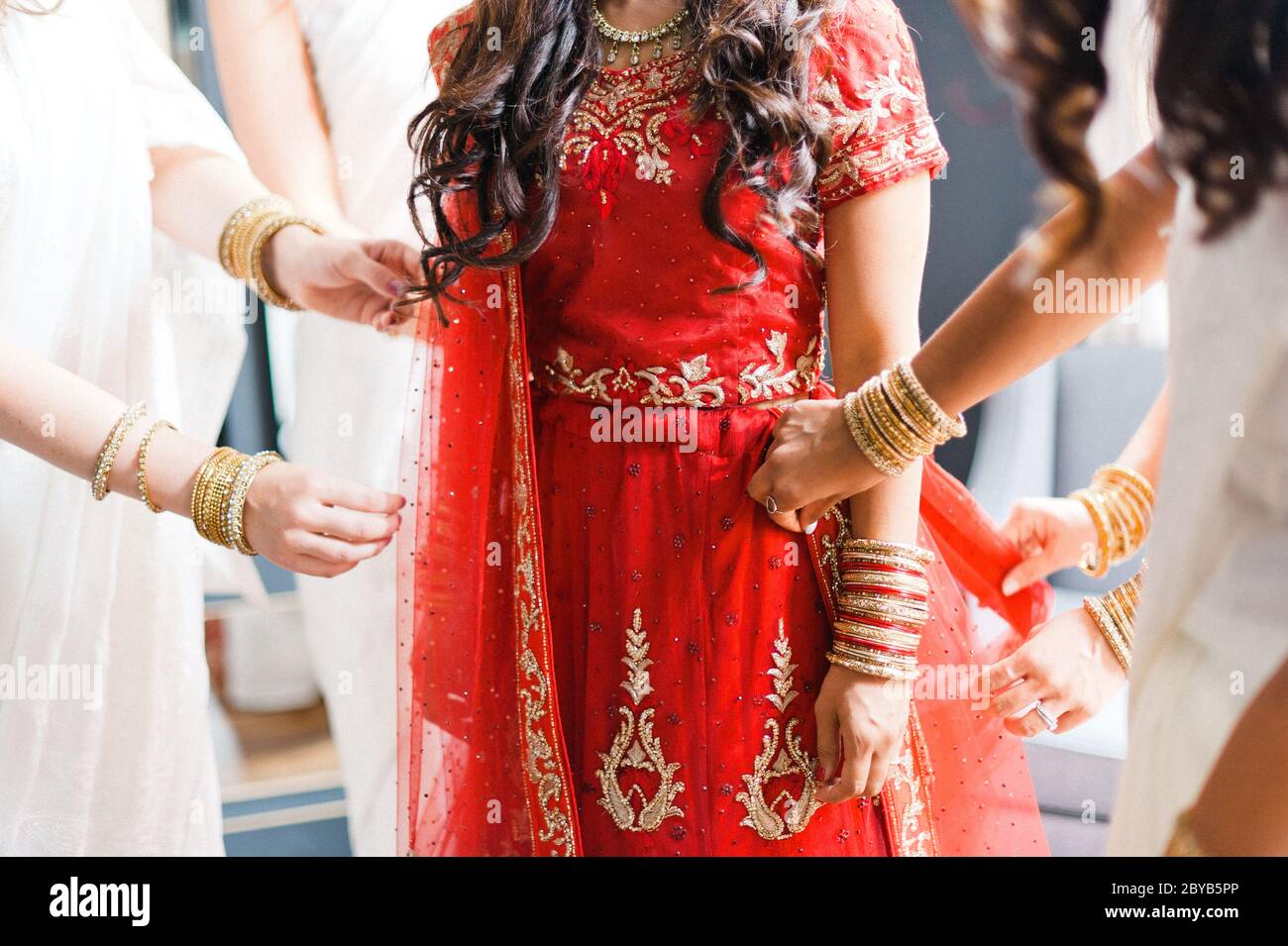 Bridemaids in weißen Sarees helfen indische Braut in rotem Kleid fertig zu machen Stockfoto