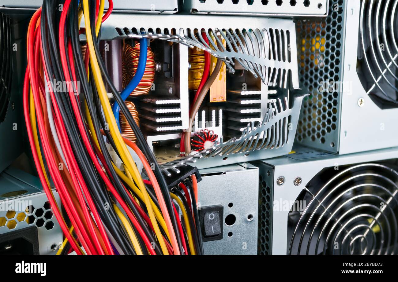 Netzteil im Inneren: Induktivitäten, Kühlkörper oder Transformator. Nahaufnahme des defekten Kästchens. Computerteil im Stapel der verwendeten Hardware. Farbige Kabel hängen. Stockfoto Netzteil im Inneren: Induktivitäten, Kühlkörper oder Transformator. Nahaufnahme des defekten Kästchens. Computerteil im Stapel der verwendeten Hardware. Farbige Kabel hängen. Stockfoto
