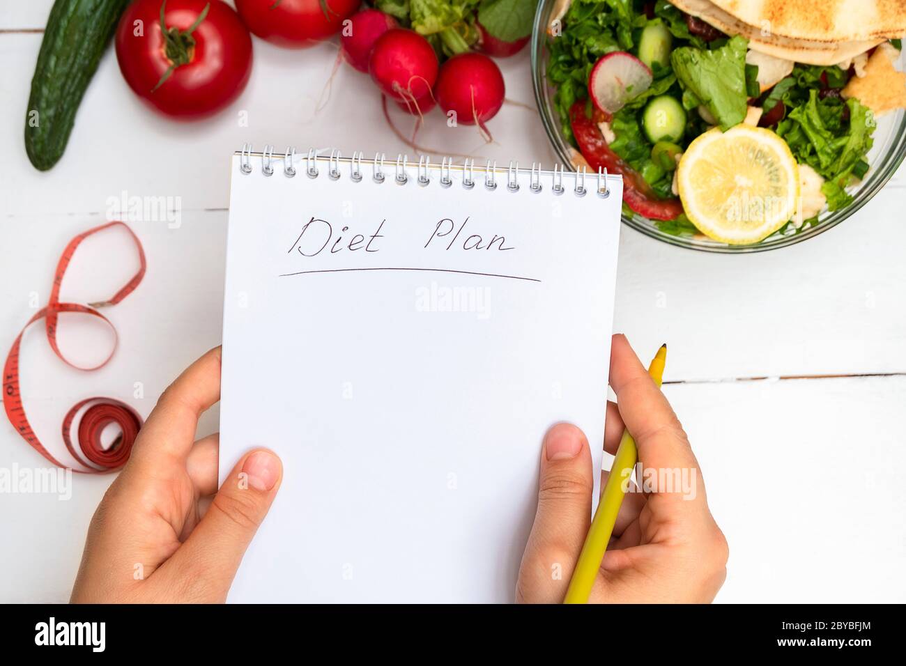 Draufsicht der Frau Hände halten Notizblock mit handgeschriebenen Worten Diät-Plan über weißem Tisch mit Gemüse und Salat Stockfoto