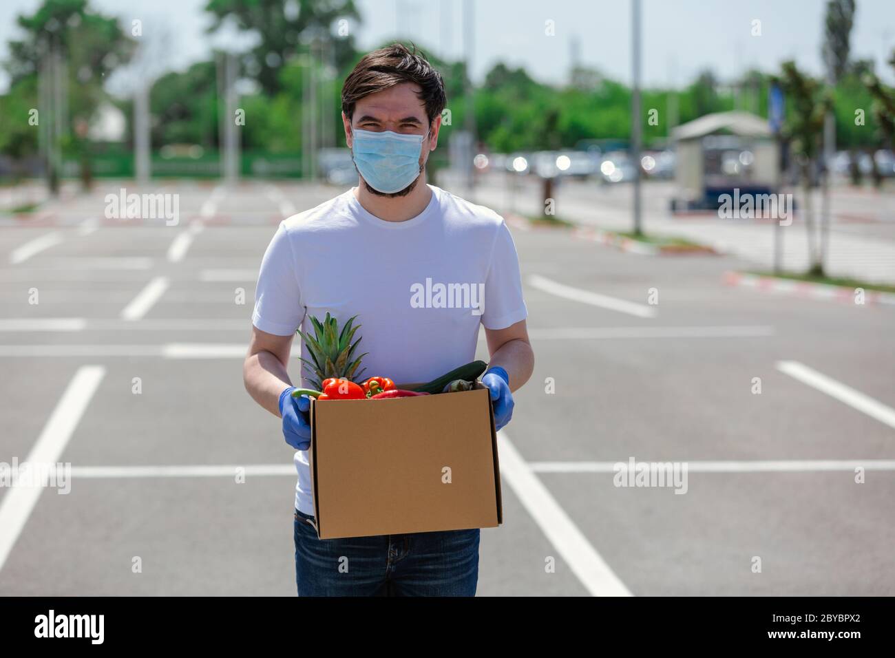 Portrait eines hübschen jungen Kuriers mit medizinischen Handschuhen und Maske liefert Essen zum Mitnehmen. Lieferdienst unter Quarantäne, Krankheitsausbruch, Stockfoto