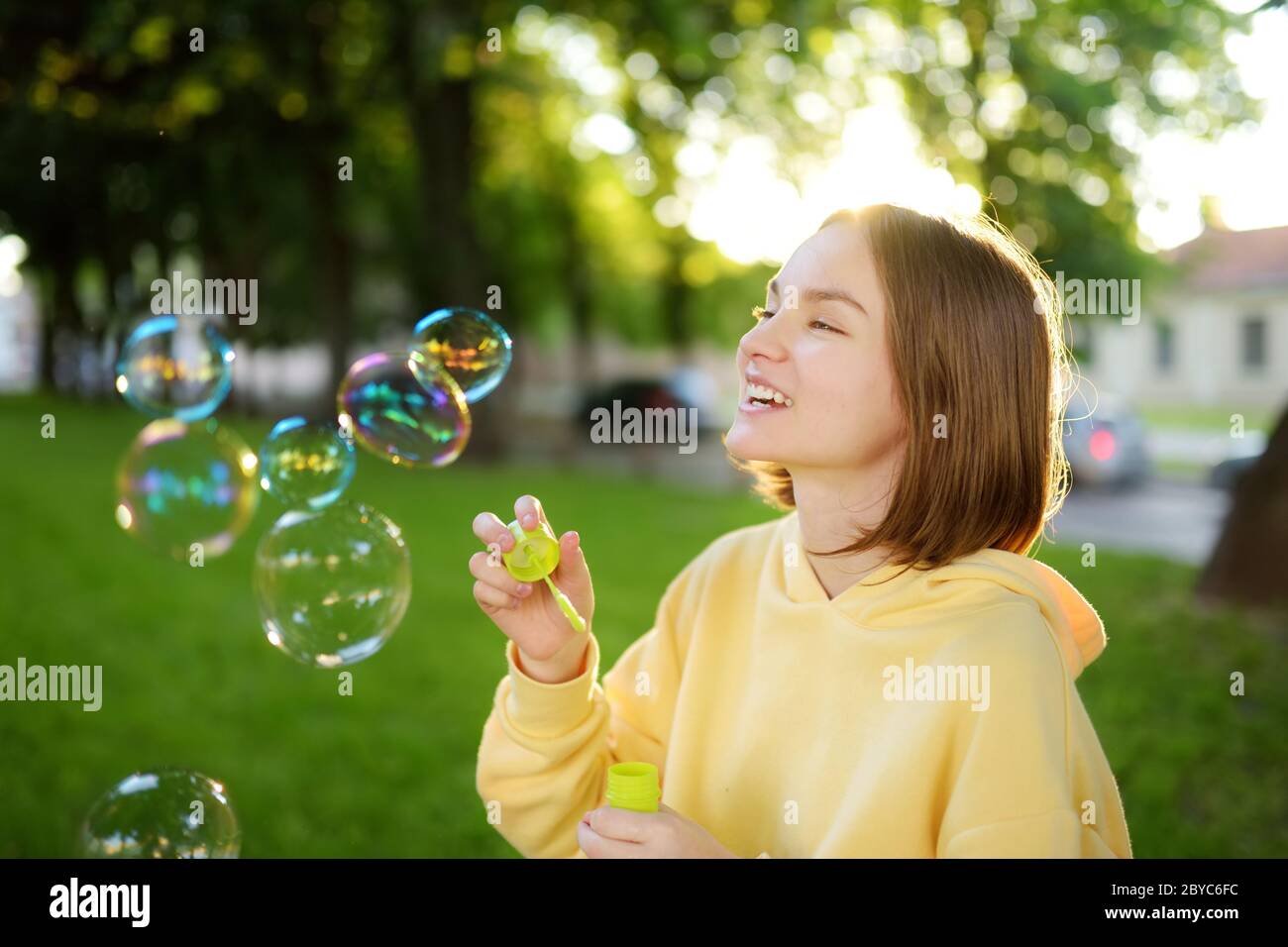 Hübsches Teenager-Mädchen, das Seifenblasen auf einem Sonnenuntergang bläst. Kinder, die im Sommer Spaß in einem Park haben. Lustige Aktivitäten für Kinder. Stockfoto