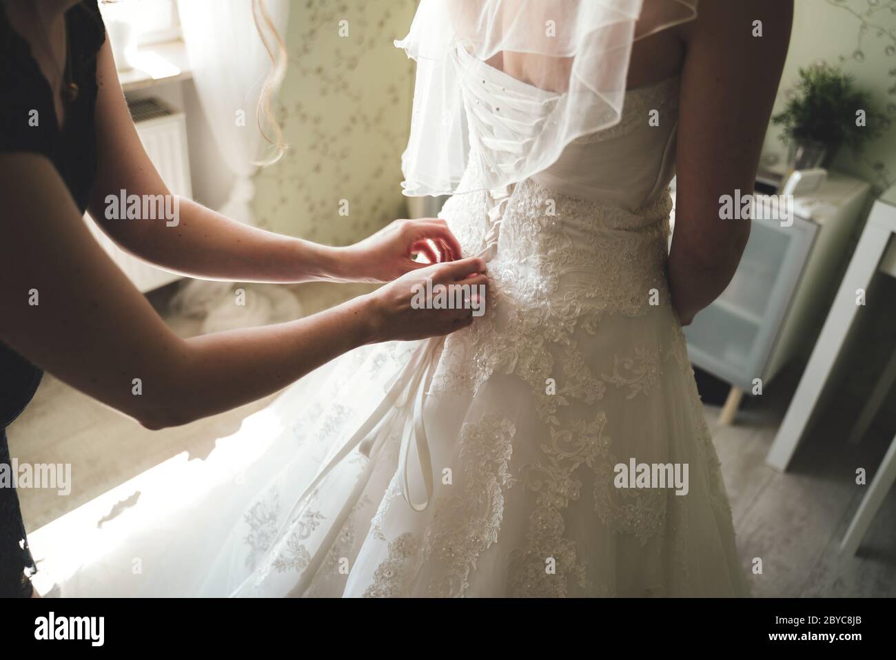 Nahaufnahme des Brautkorsetts. Rückansicht auf Braut in weißem Brautkleid. Brautjungfer helfen Braut Hochzeitskleid zu kleiden. Konzept für Hochzeitstag. Stockfoto