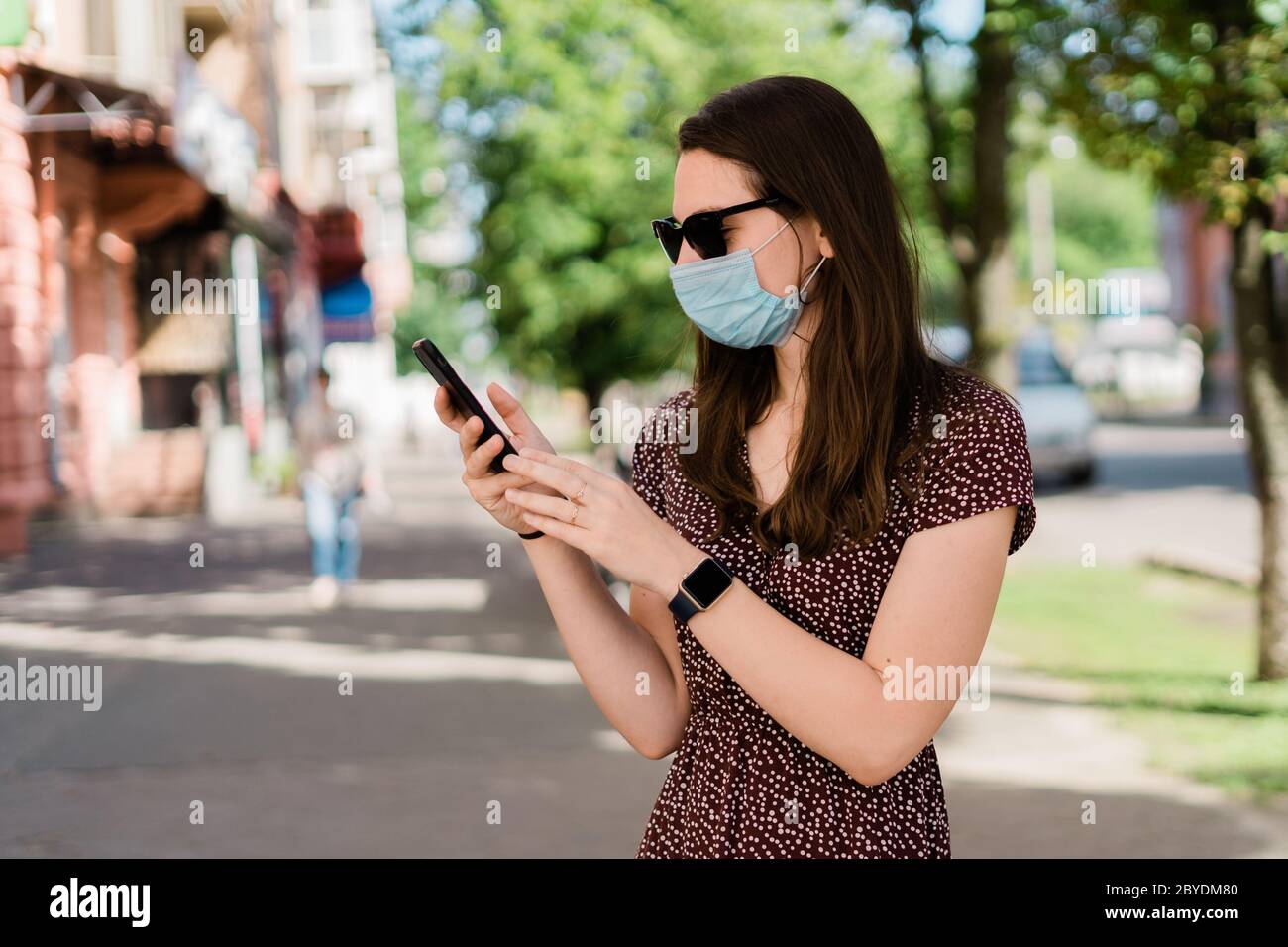 Junge Frau mit medizinischer Maske und Telefon. Sommer im Freien neuen normalen Lebensstil Stockfoto