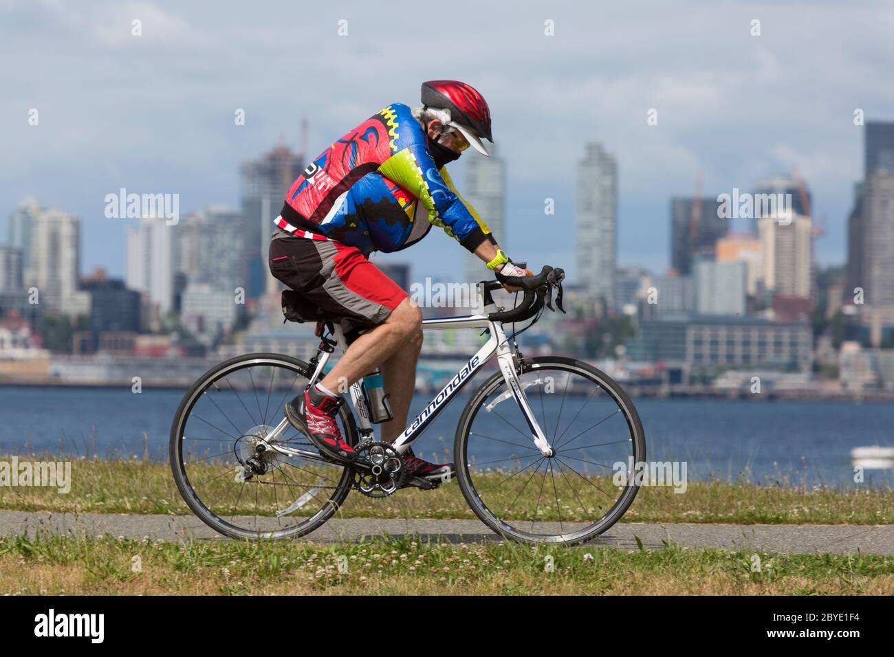 Ein Radfahrer mit einer schützenden Gesichtsmaske fährt an einem sonnigen Nachmittag in Seattle, Washington, entlang des Alki Trail. Stockfoto