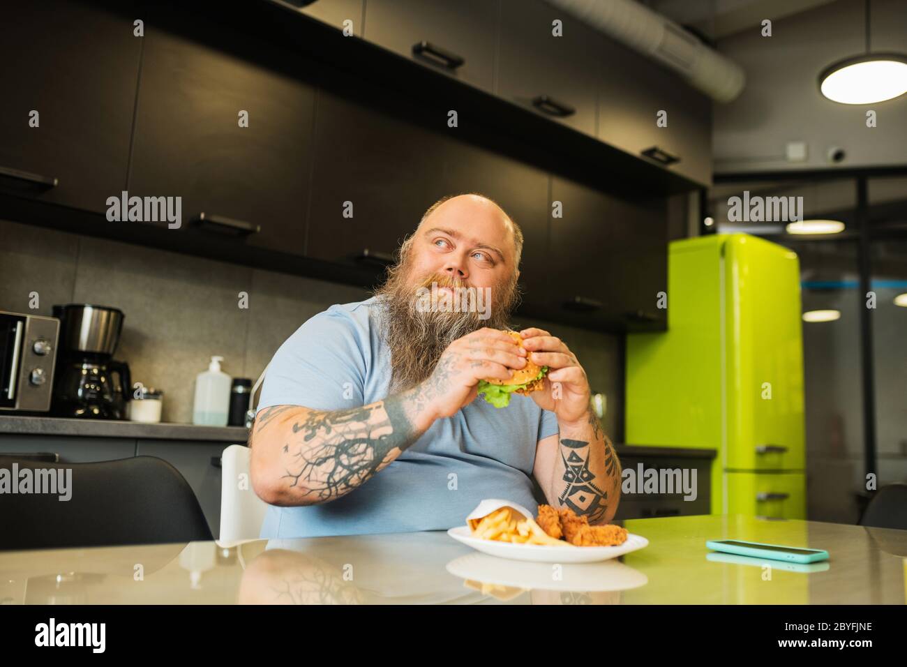 Glücklicher großer Mann mit Burger in den Händen am Tisch Stockfoto