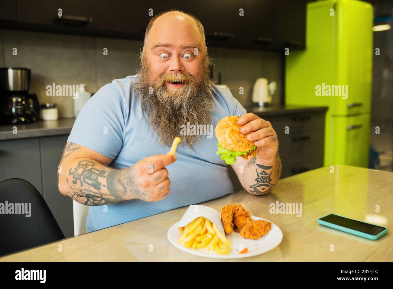 Ein fetter, begeisterter Mann mit einem Burger und pommes frites. Stockfoto