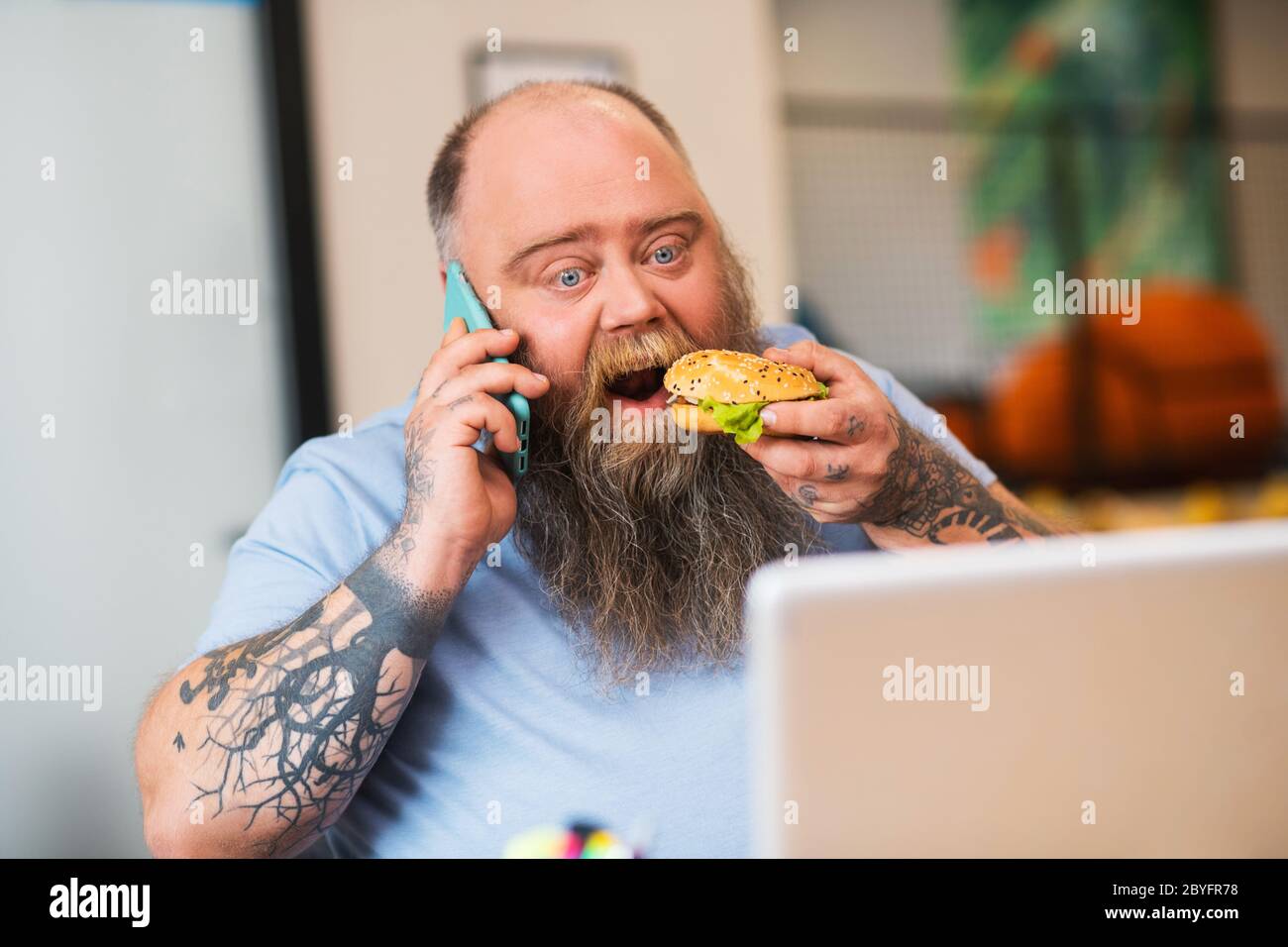 Kahlköpfiger Mann, der am Telefon telefoniert und einen Burger isst Stockfoto