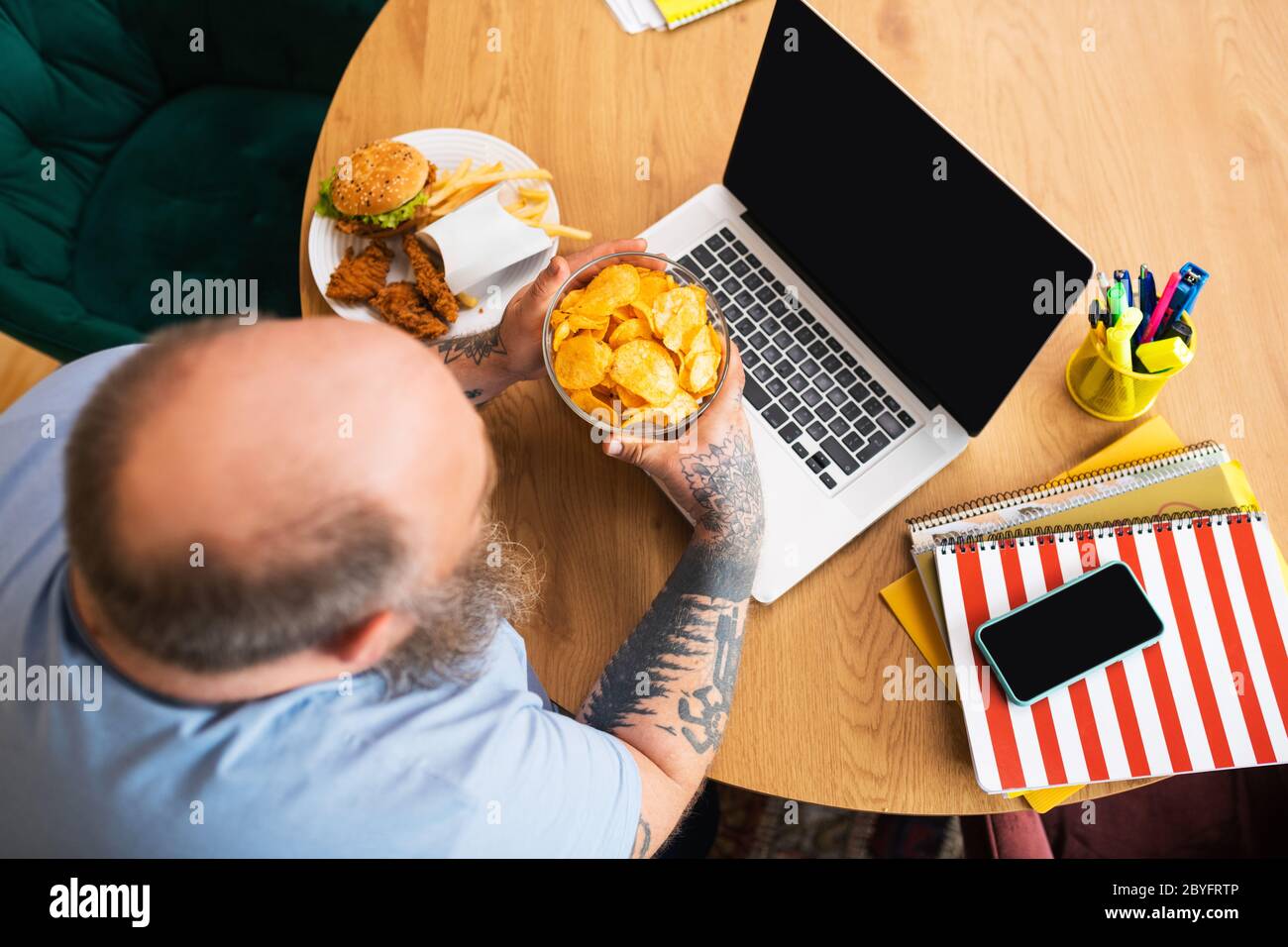 Glatze Mann sitzt am Tisch und hält einen Teller mit Chips Stockfoto
