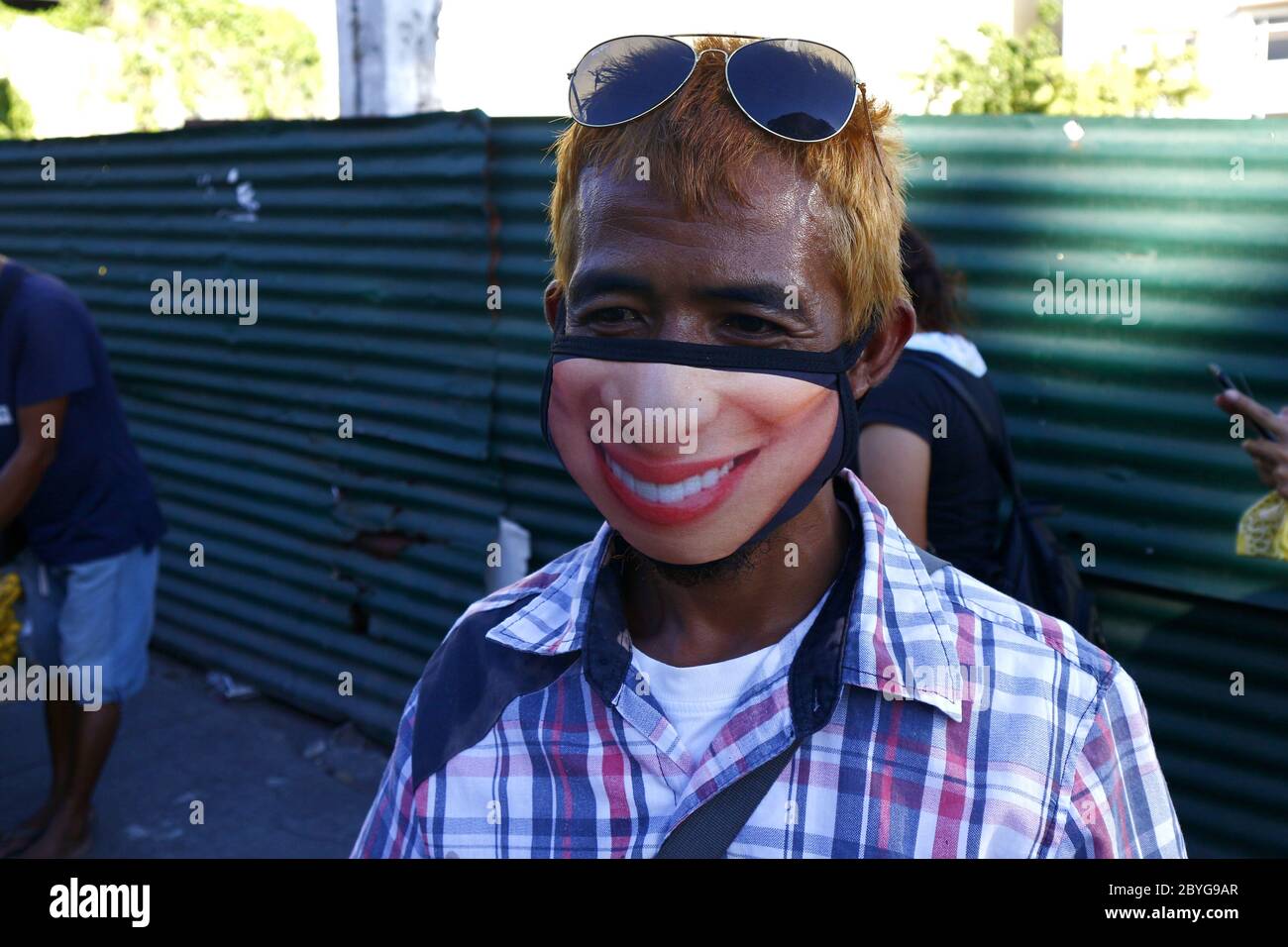 Antipolo City, Philippinen - 6. Juni 2020: Erwachsene philippinische Mann verwenden eine waschbare Gesichtsmaske mit einem lustigen Gesicht auf sie gedruckt während der Covid 19 Virus outbr Stockfoto