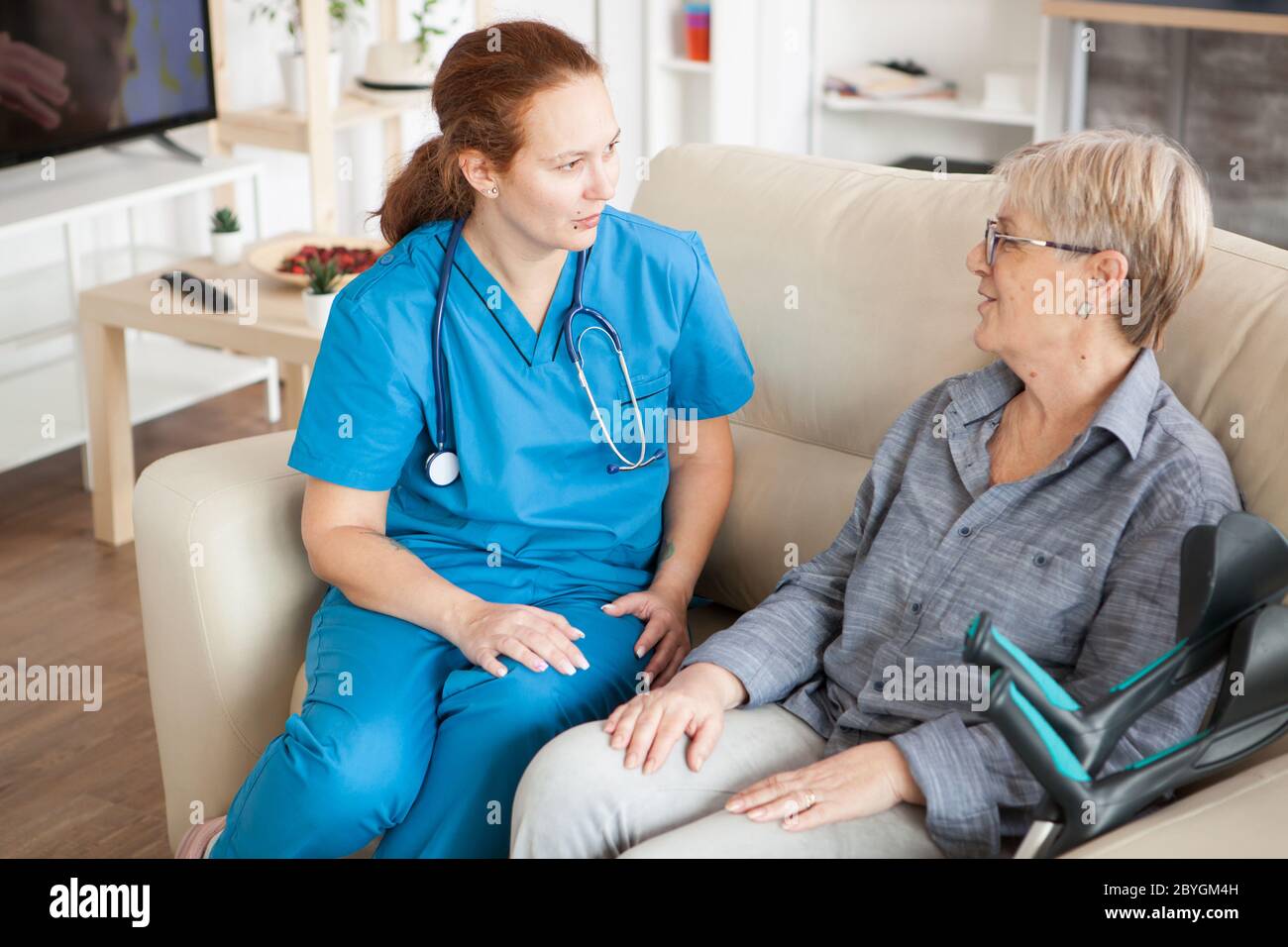 Gesundheitsgast mit Stethoskop auf einer Couch im Pflegeheim im Gespräch mit einer alten Frau. Stockfoto