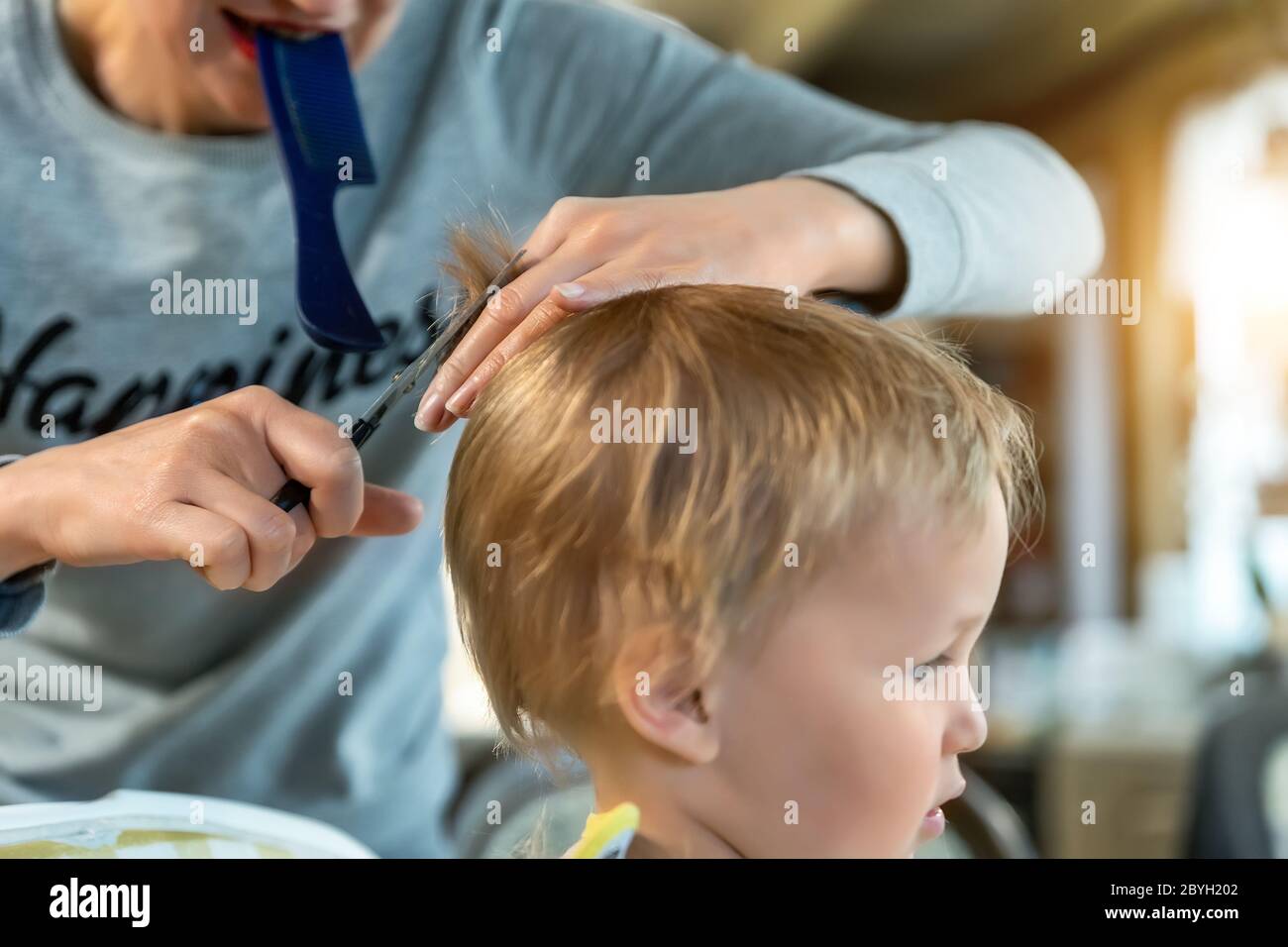 Close-up junge Erwachsene kaukasische Mutter machen Haarschnitt fot niedlich liebenswert Sohn Kleinkind Junge zu Hause durch Quarantäne und Sperrung. Mutter schneiden Haare des Kindes Stockfoto