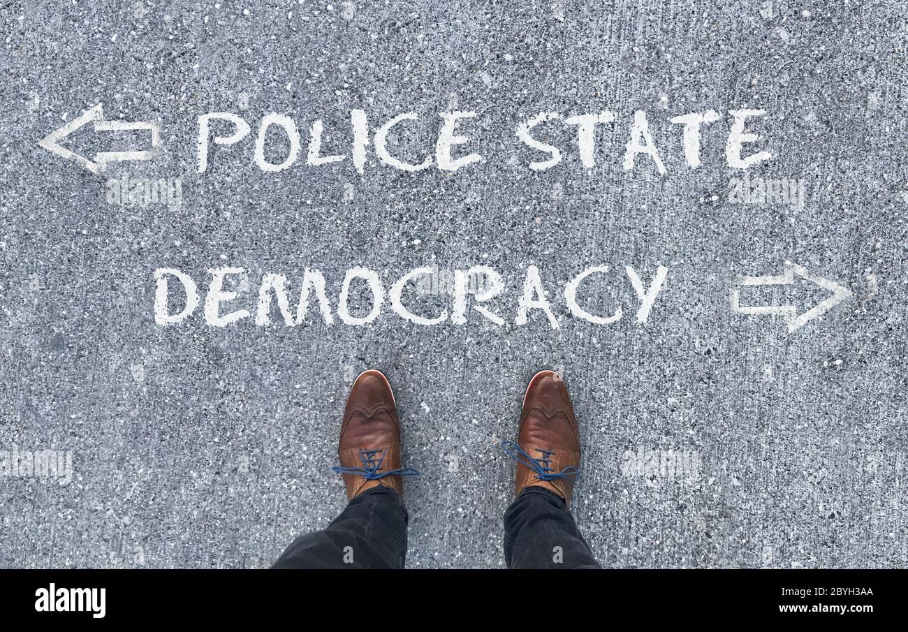 Draufsicht auf einen Mann, der vor den Worten "Polizeistaat" und "Demokratie" steht, mit Pfeilen, die nach links und rechts zeigen Stockfoto