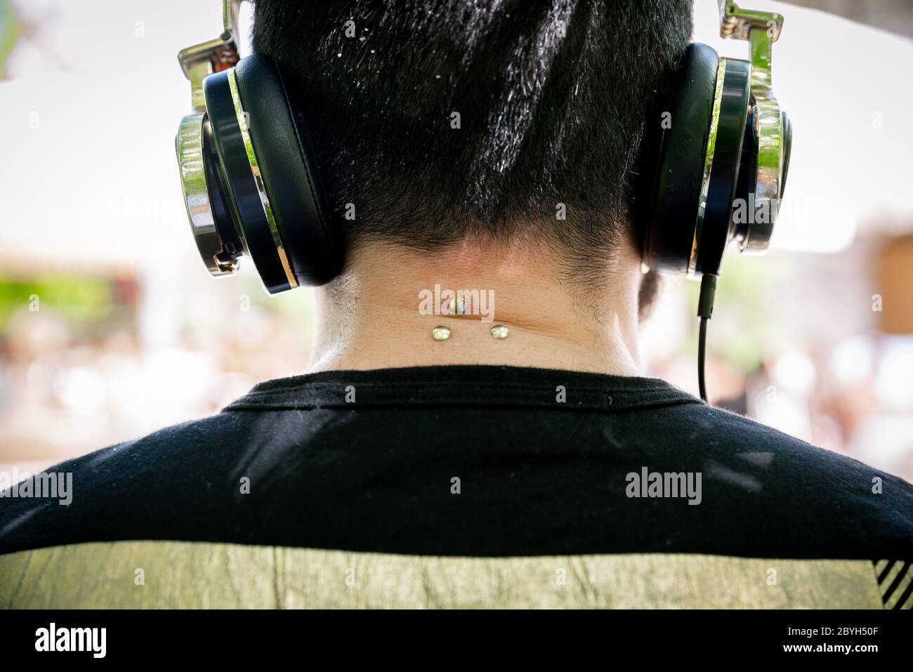 Der junge DJ von hinten spielt Musik mit Kopfhörern an den Ohren, mit Piercings am Nacken. Stockfoto