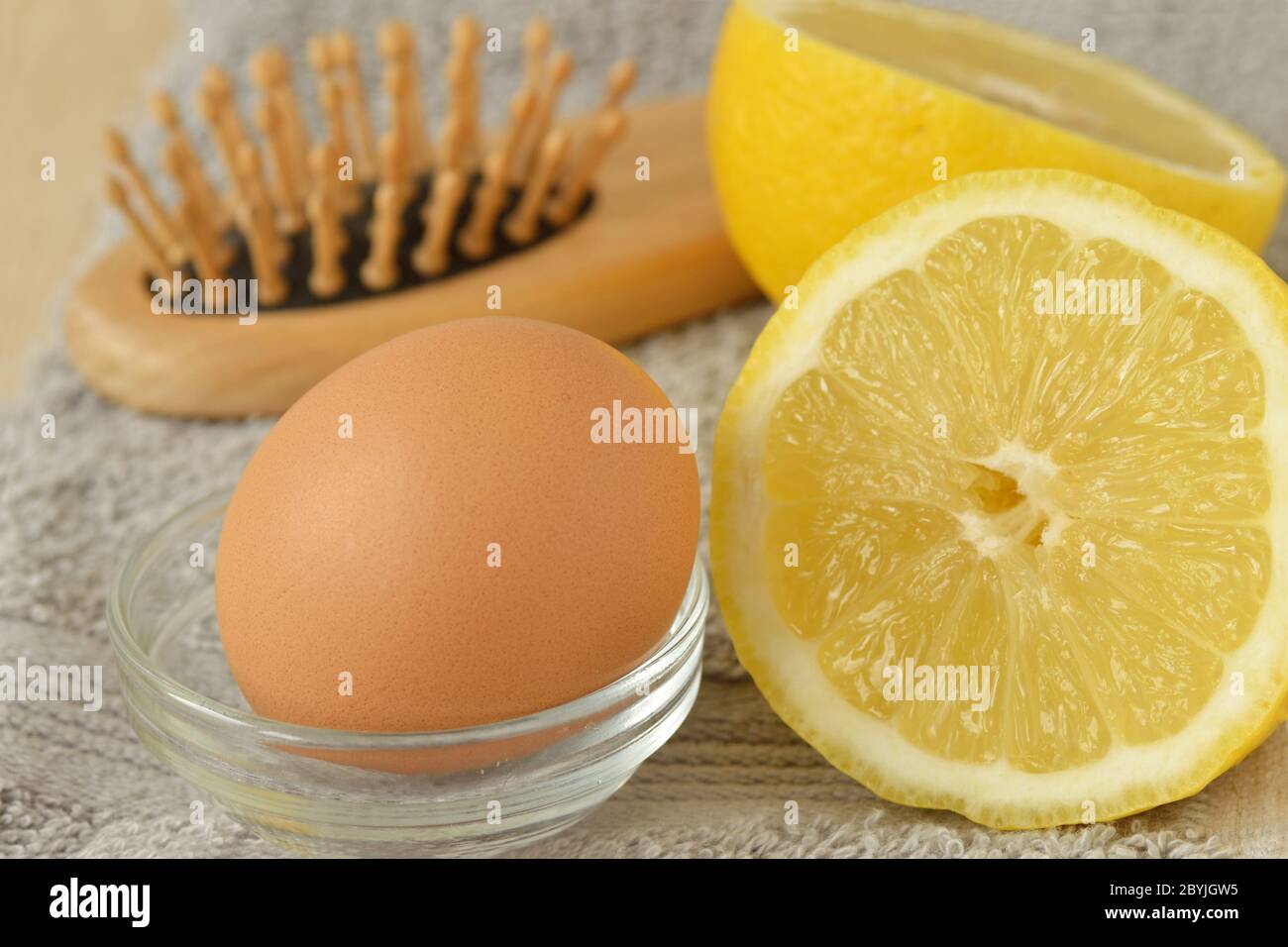 Ei und Zitrone mit Haarbürste auf grauem Handtuch - hausgemachte Haarmaske Zutaten Stockfoto