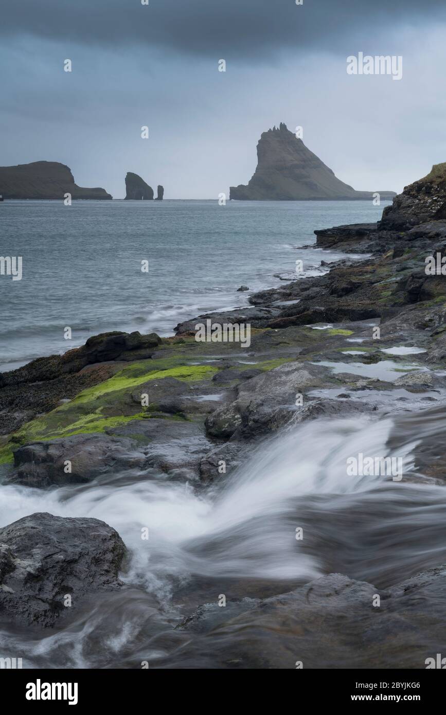 Klassische Landschaft der Färöer Inseln mit hohen Klippen, Inseln, Bergen, Wasserfällen und Fjorden. Drangarnir und Tindhólmur am Horizont Stockfoto