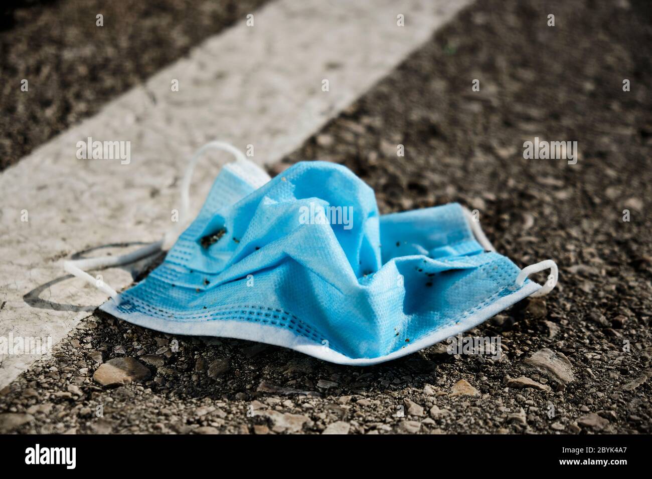 Nahaufnahme einer blauen chirurgischen Maske auf dem Asphalt einer Straße, eines Parkplatzes oder einer Straße geworfen Stockfoto