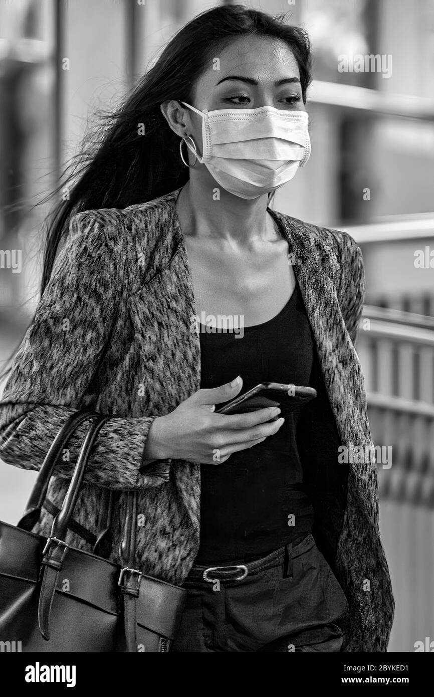 Attraktive Frau mit Gesichtsmaske und Handy während der Covid-Pandemie, Bangkok, Thailand Stockfoto