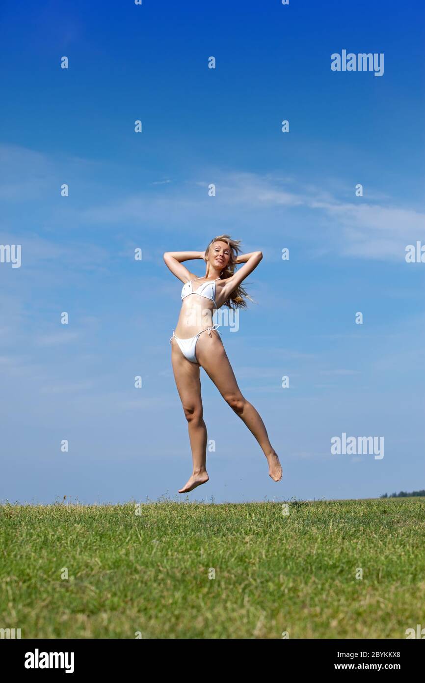 Die glückliche Frau springt in einem Sommer grünen Wiese agai Stockfoto